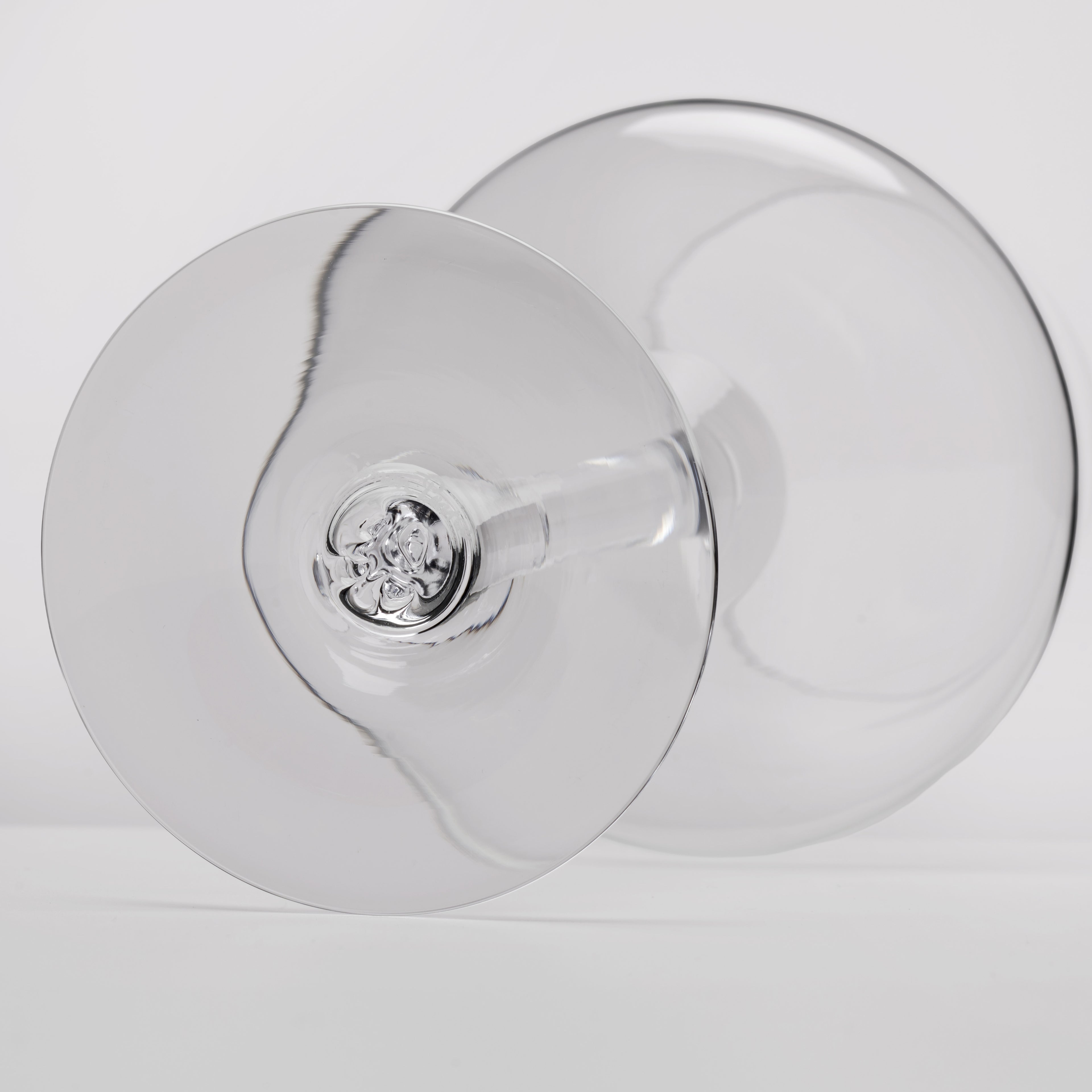 A close-up studio shot of a clear glass wine glass viewed from the bottom, showing the circular bowl and stem against a light gray background.