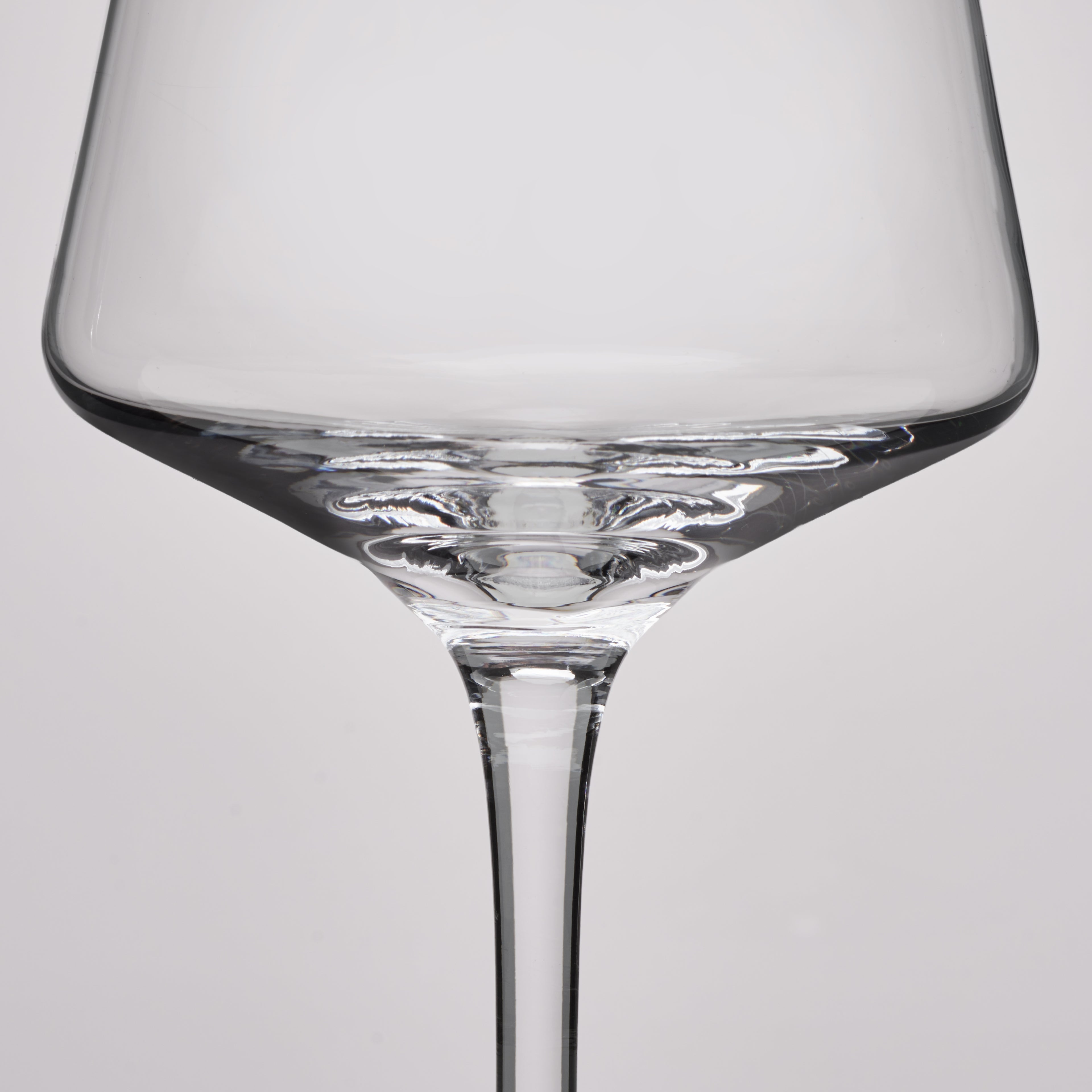 A close-up studio shot of a clear glass wine glass against a light gray background.
