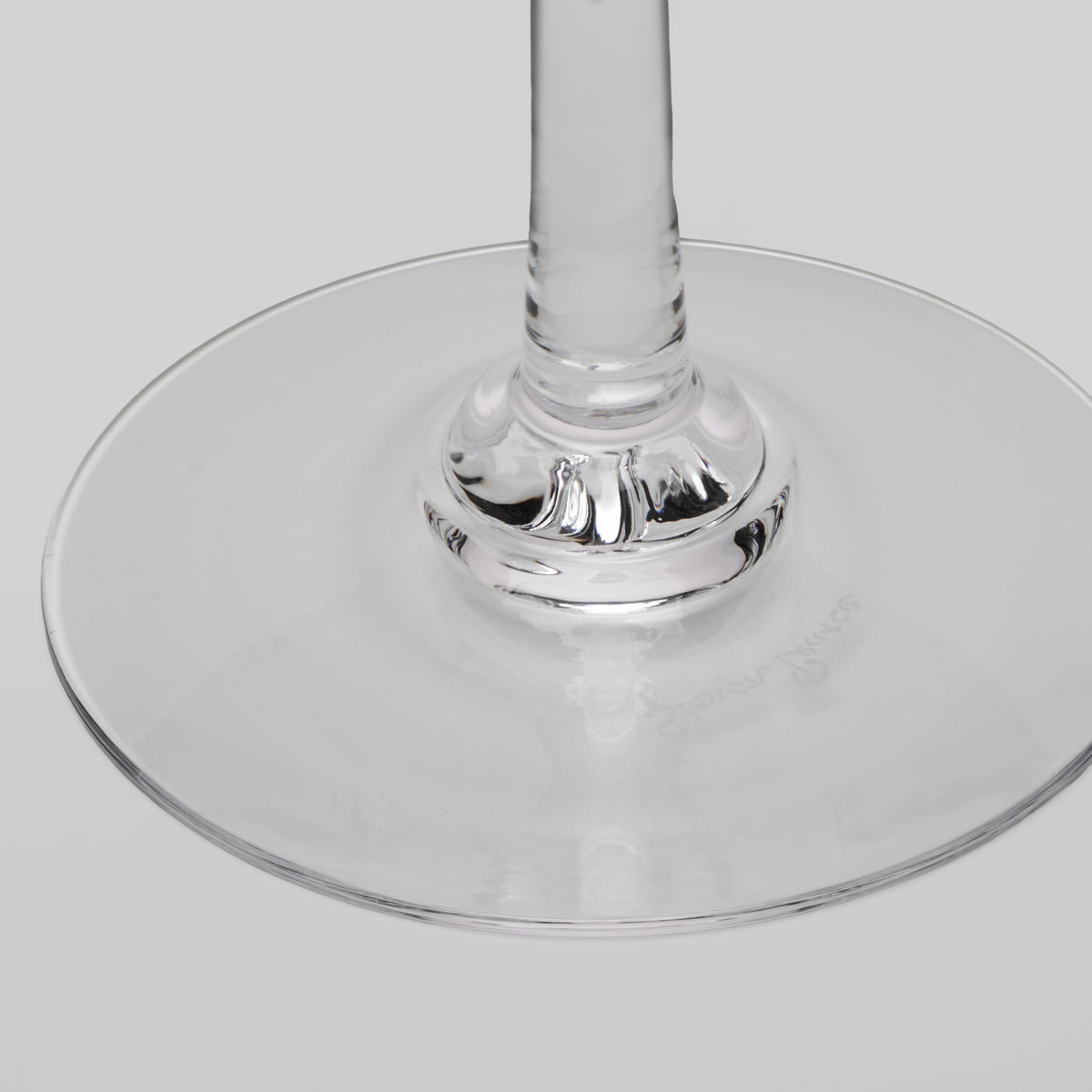 Close-up of a clear glass wine glass showing the base and stem on a light gray background.