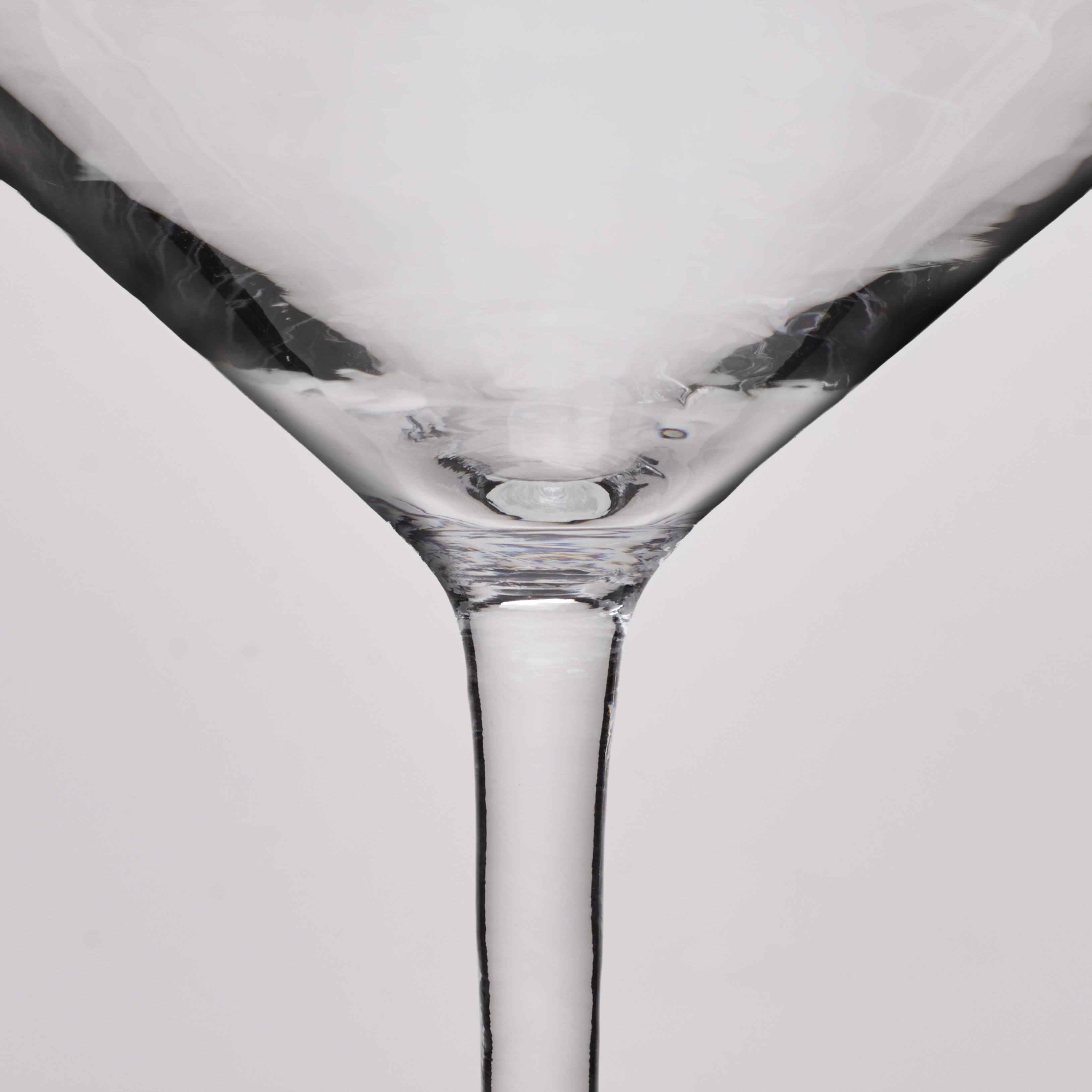 Close-up of a clear glass martini glass showing the base and stem against a light gray background.