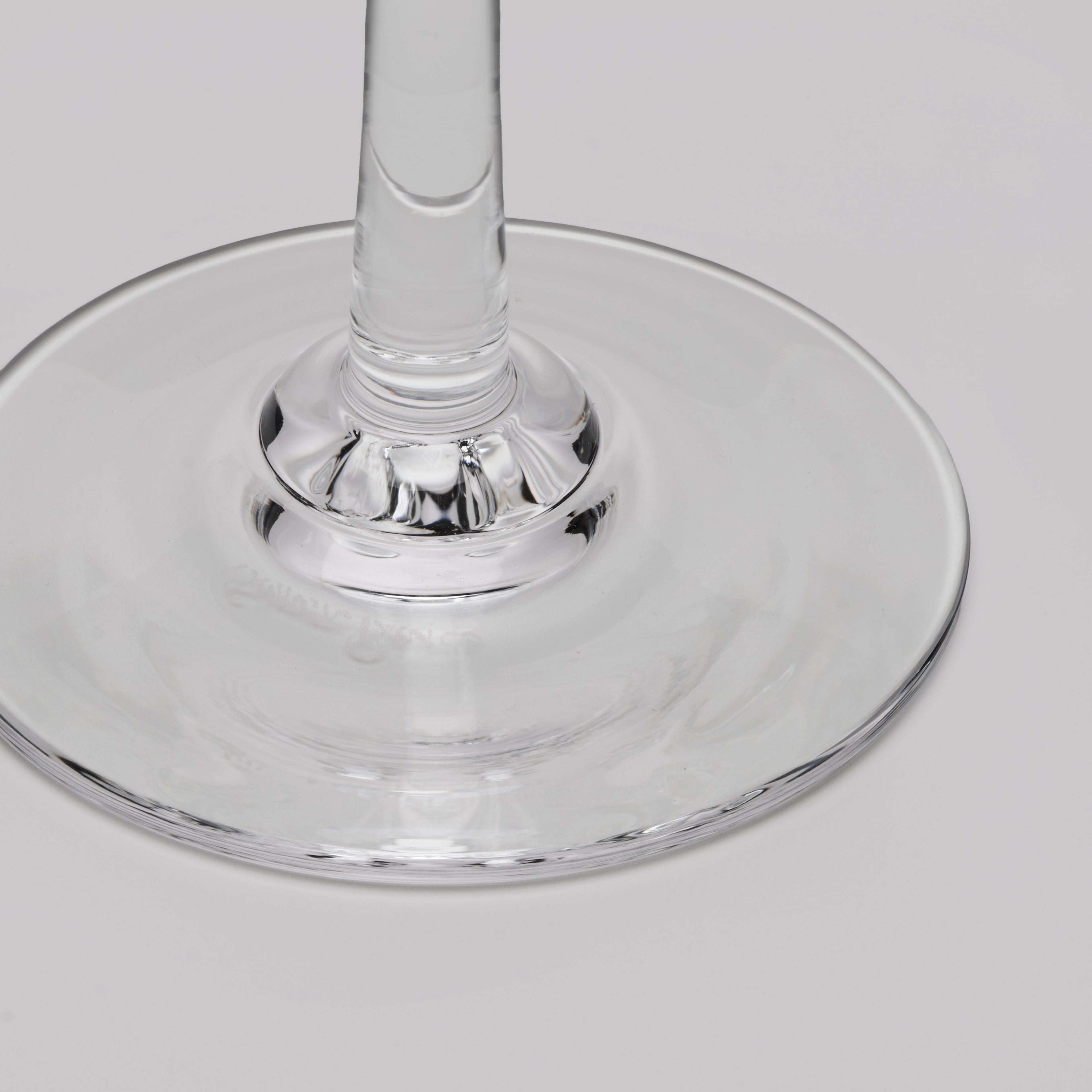 A close-up of a clear glass wine glass base and stem on a light gray background.