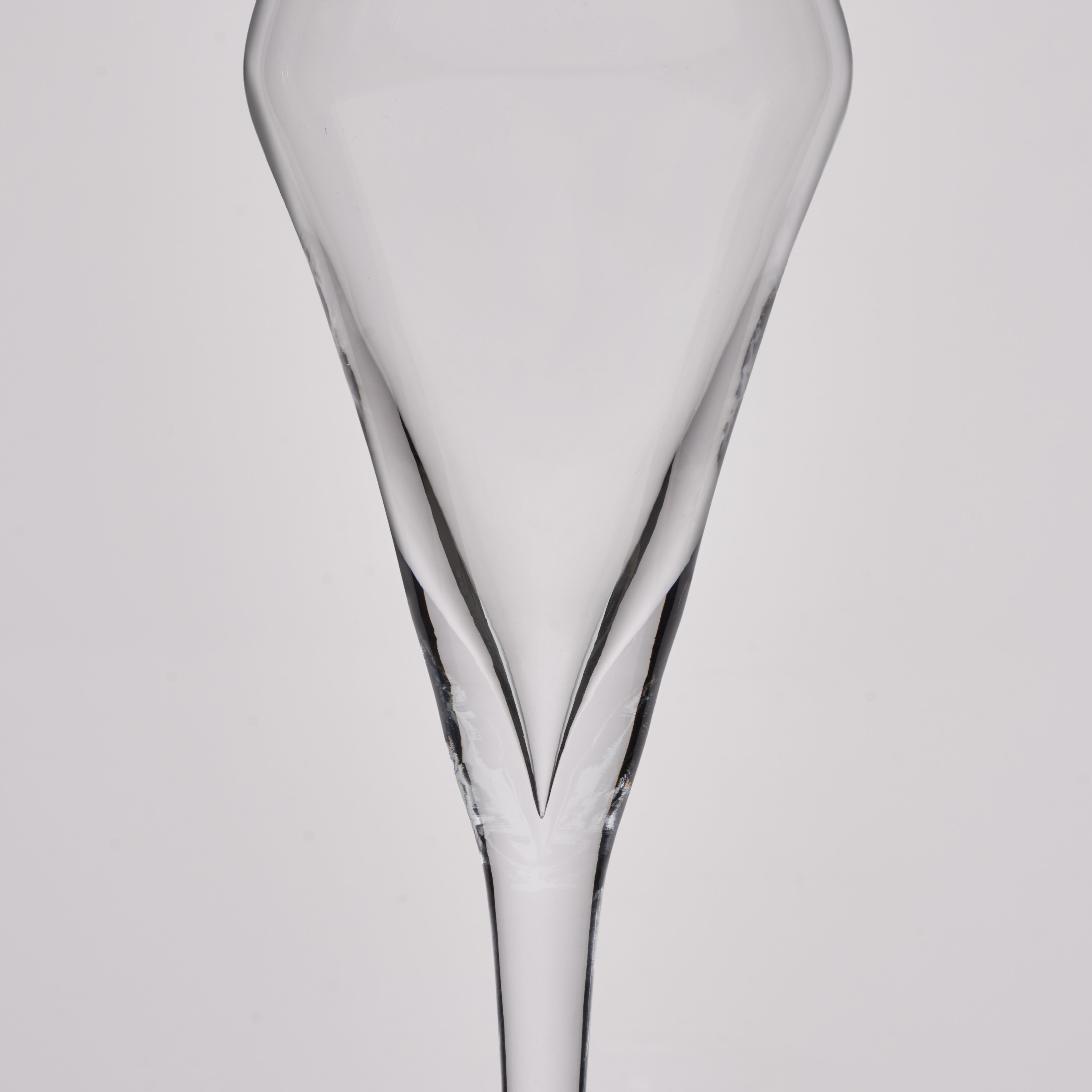 A clear glass champagne flute shown from the back against a light gray studio background.