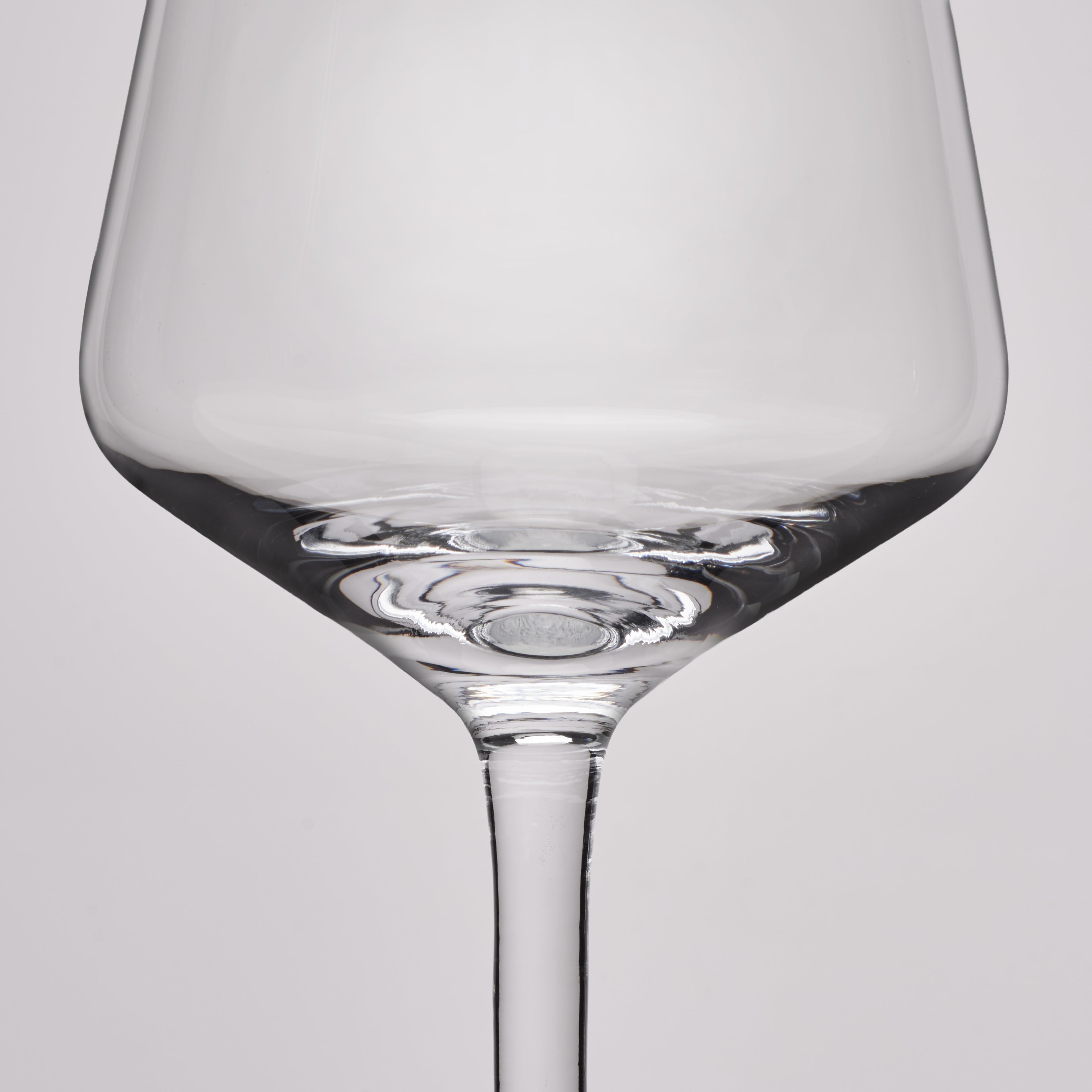 A close-up studio shot of a clear glass wine glass against a light gray background.