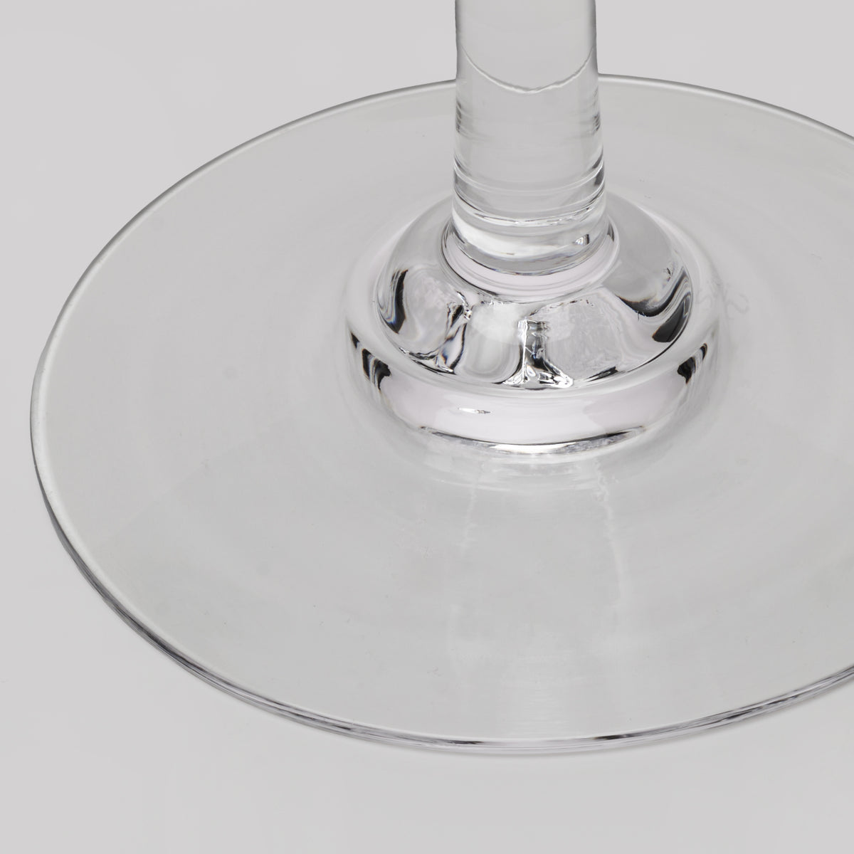 Close-up of a clear glass wine glass base and stem on a light gray background.