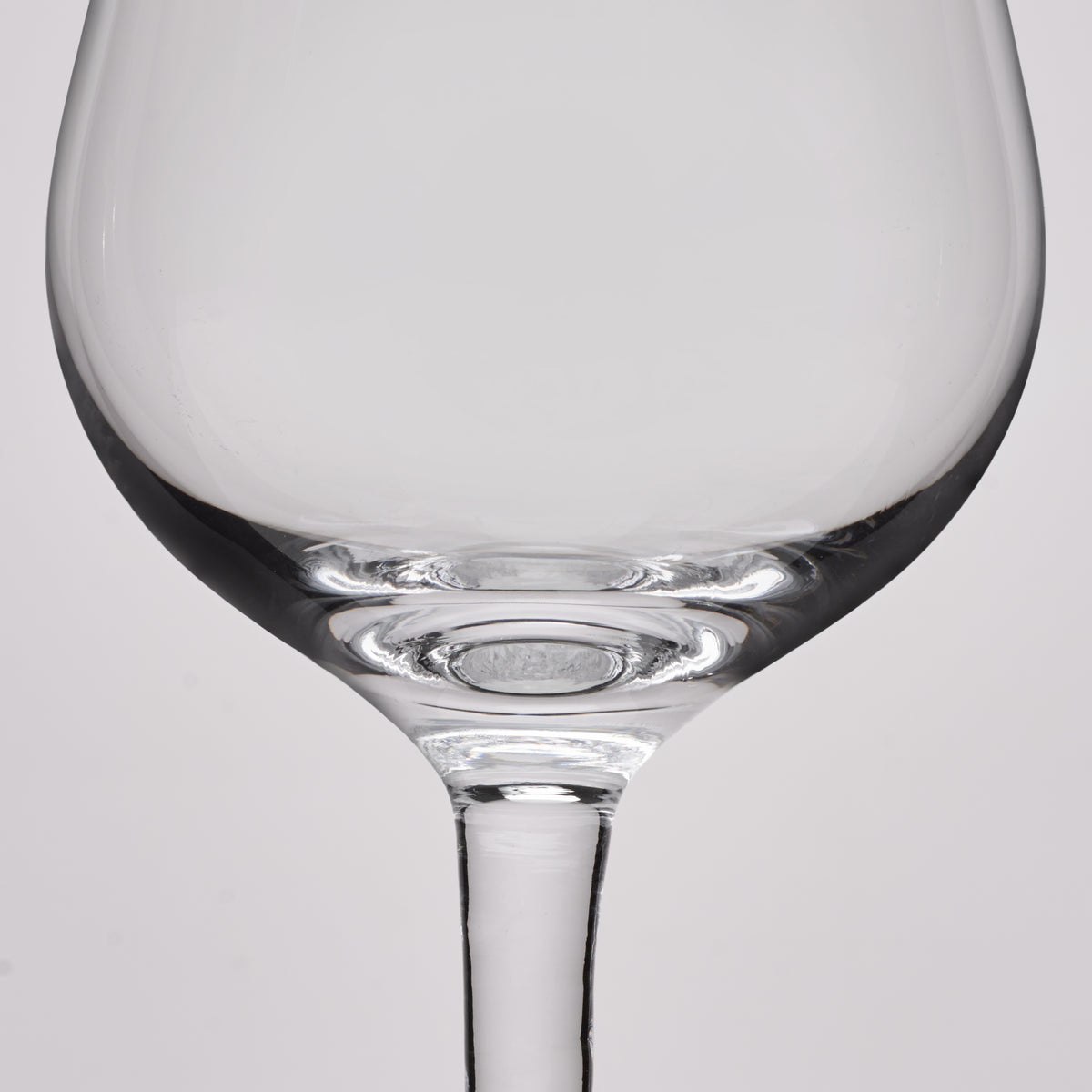 Close-up of a clear glass wine glass showing the bowl base and stem against a light gray background.