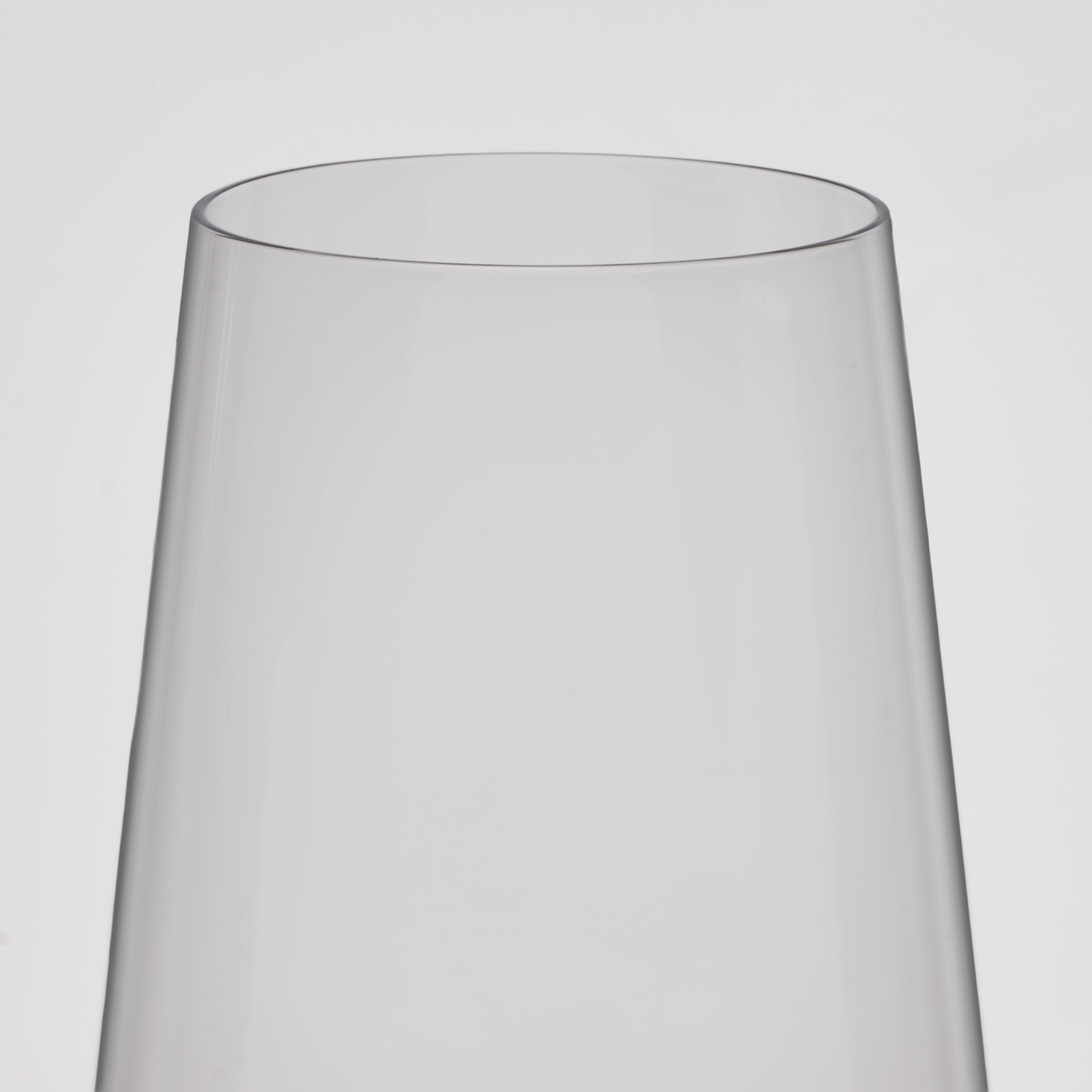 A close-up of a clear wine glass with a flared, tapered rim, shown against a plain light gray background.