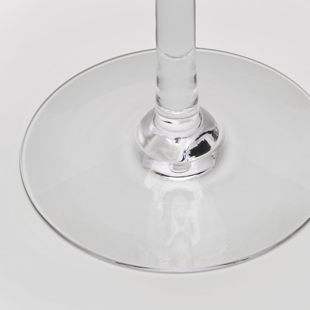 Close-up of a clear wine glass base and a central stem on a light gray background.