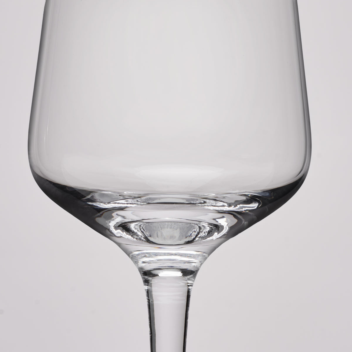 A close-up studio shot of a clear glass wine glass against a light gray background.