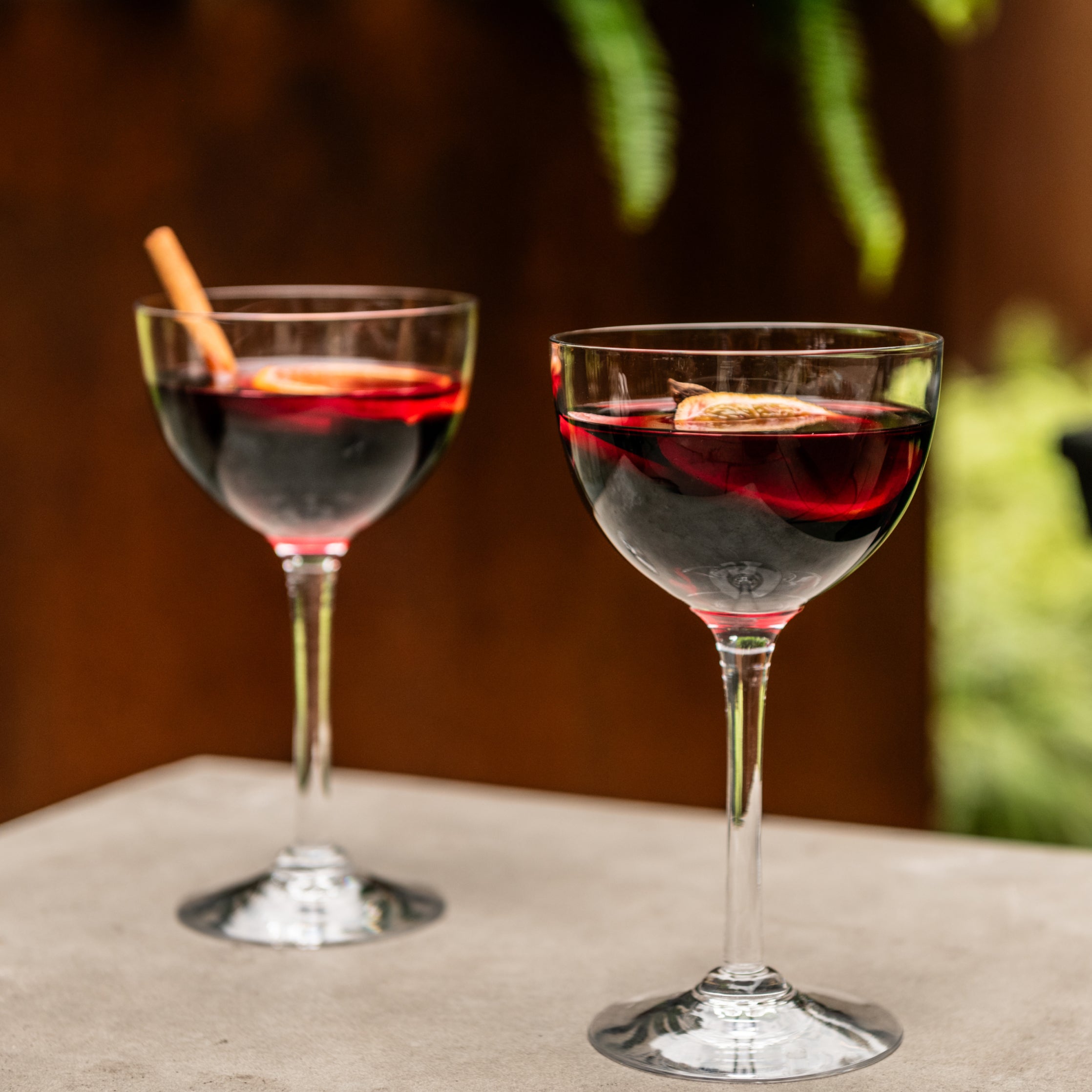 Two crystal coupe glasses filled with red cocktails and garnished with citrus wheels on a white surface.