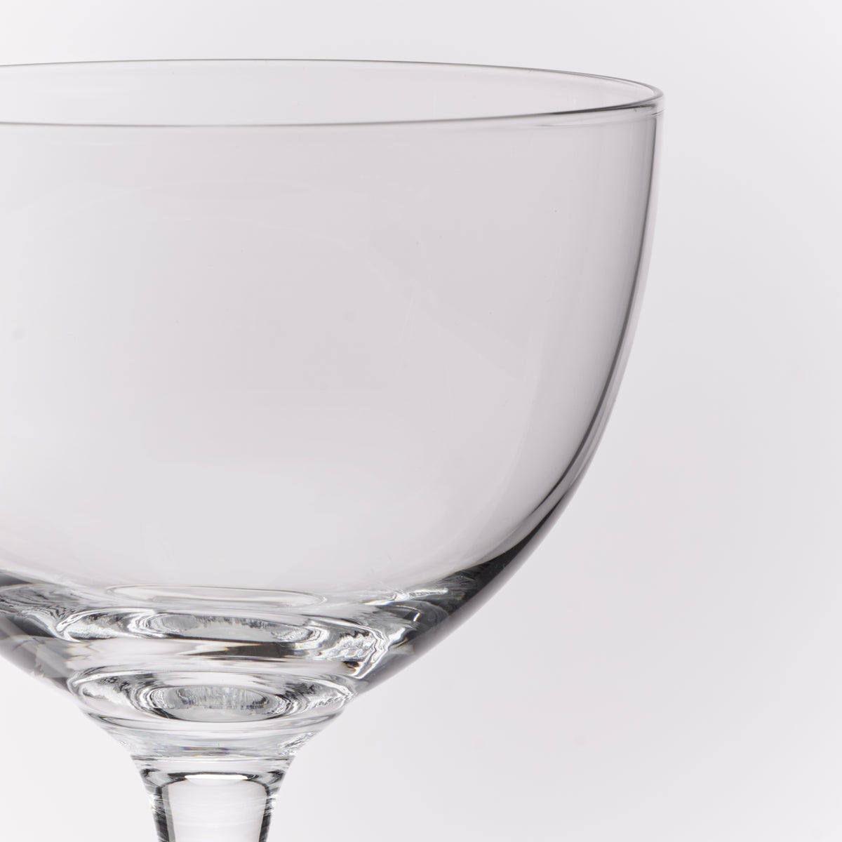 A close-up of a clear glass coupe glass on a light gray background.