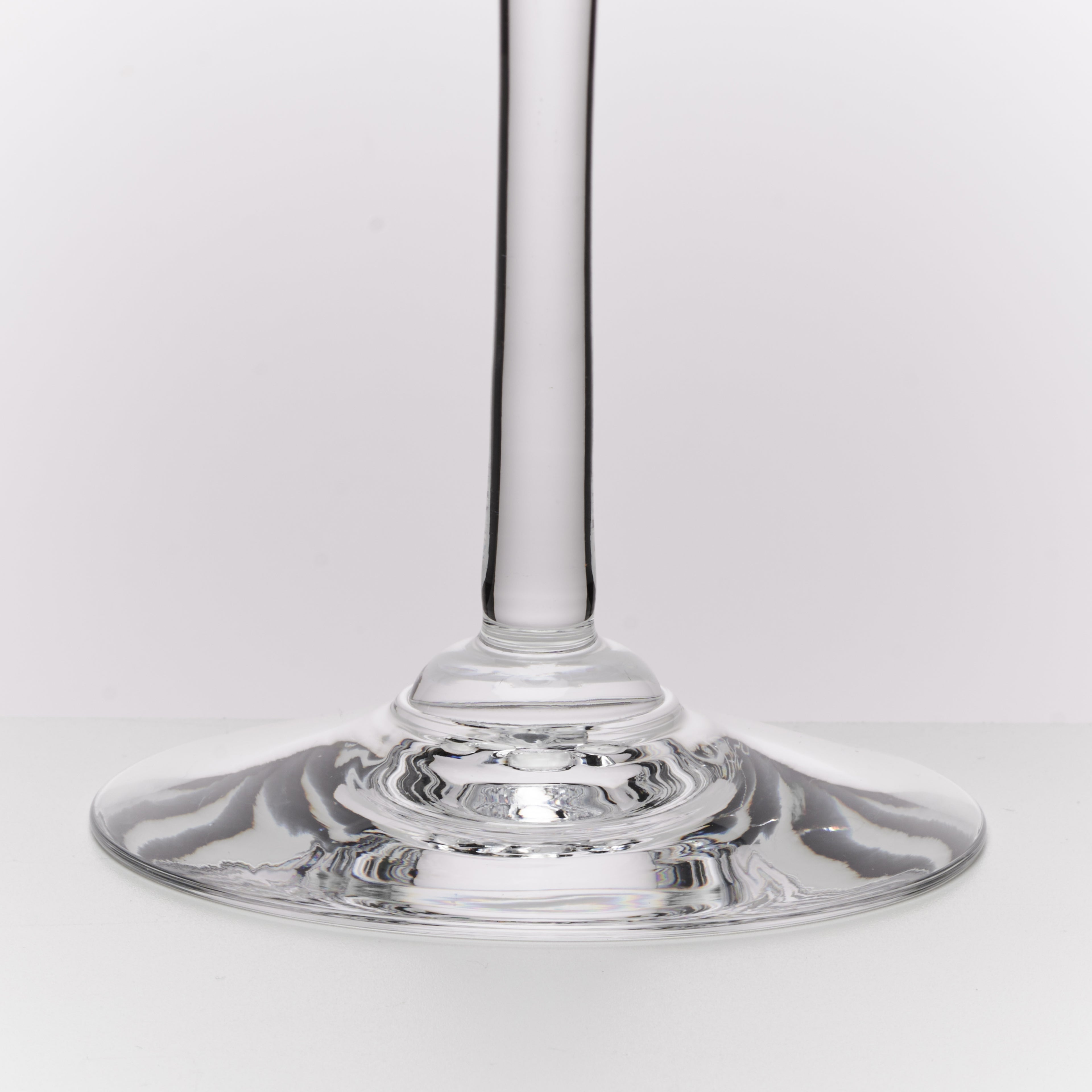 A close-up studio shot of a clear glass wine glass stem and wide circular base on a light gray background.