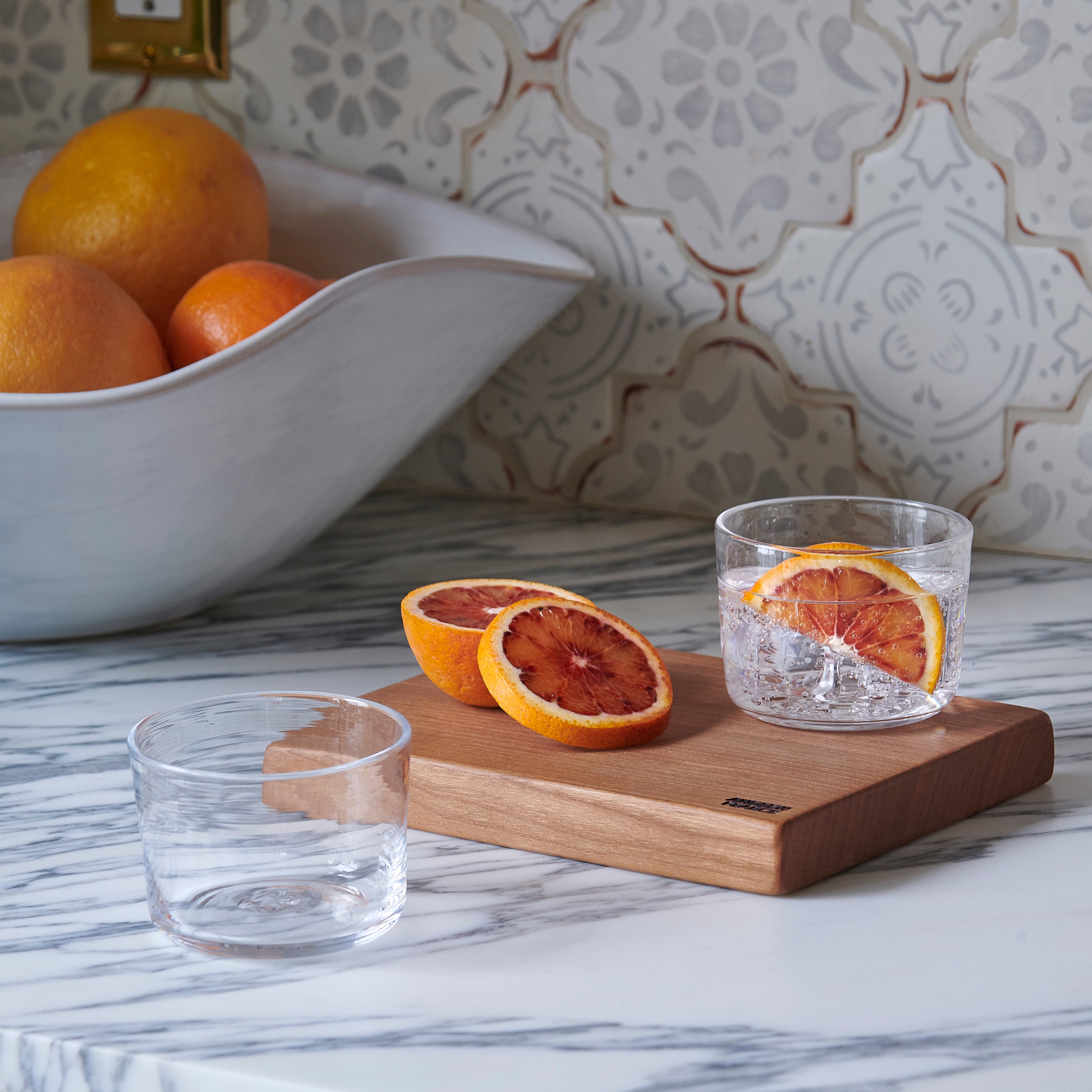 Four clear glass tumblers with grapefruit slices and ice, displayed on a wooden board.