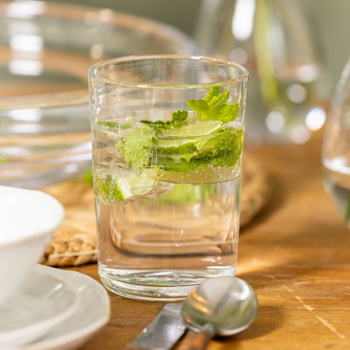 Clear glass tumbler filled with water, ice, and fresh mint leaves on a wooden table.