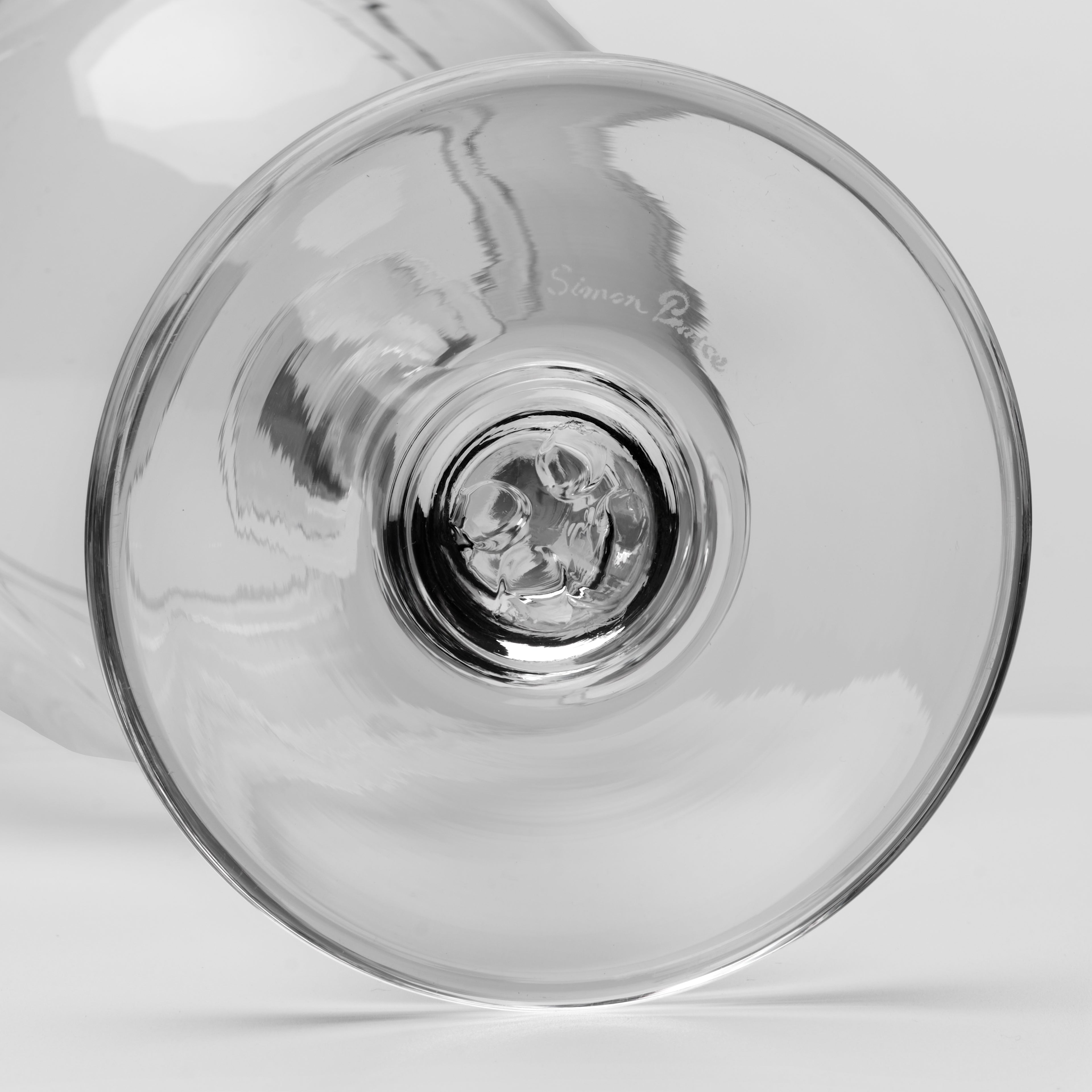 Close-up of a clear glass viewed from the bottom, showing the circular base and subtle etched brand text on the glass against a light gray background.