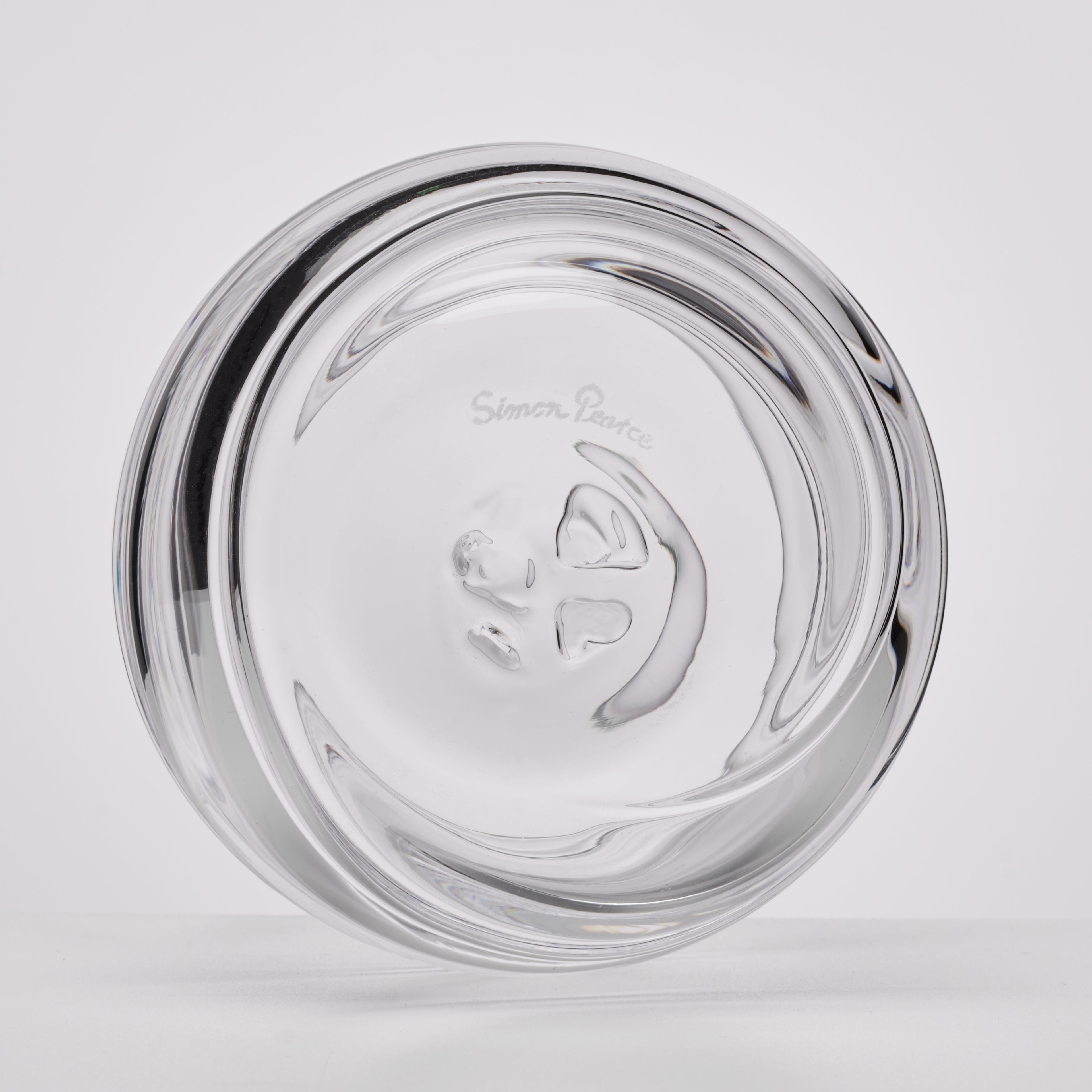A clear glass ashtray with a sculptural, wavy design and the etched brand name Simon Pearce visible in the center, shown on a light gray background.