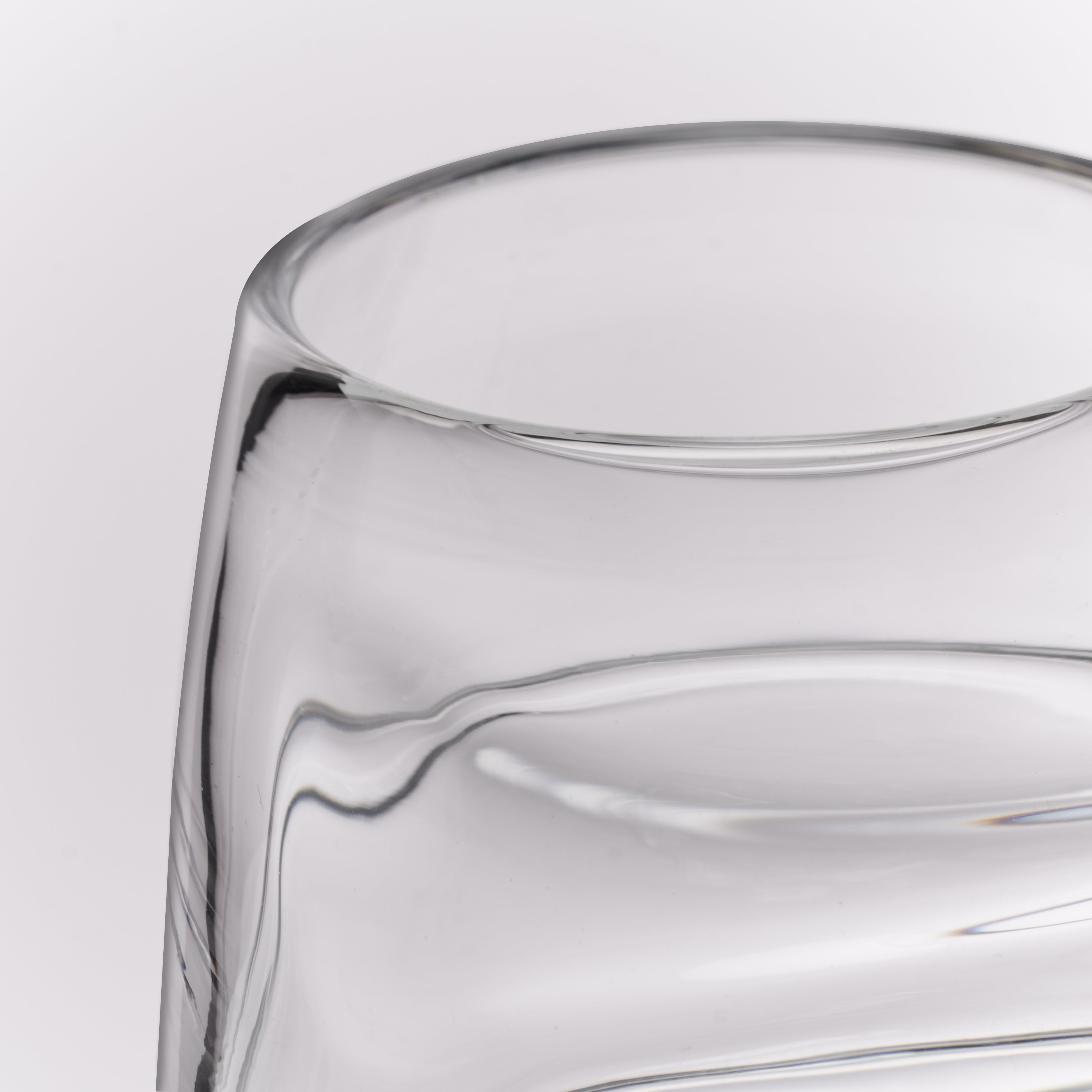 Close-up of a clear glass tumbler with a thick, rounded rim and smooth curved glass body on a light gray background.