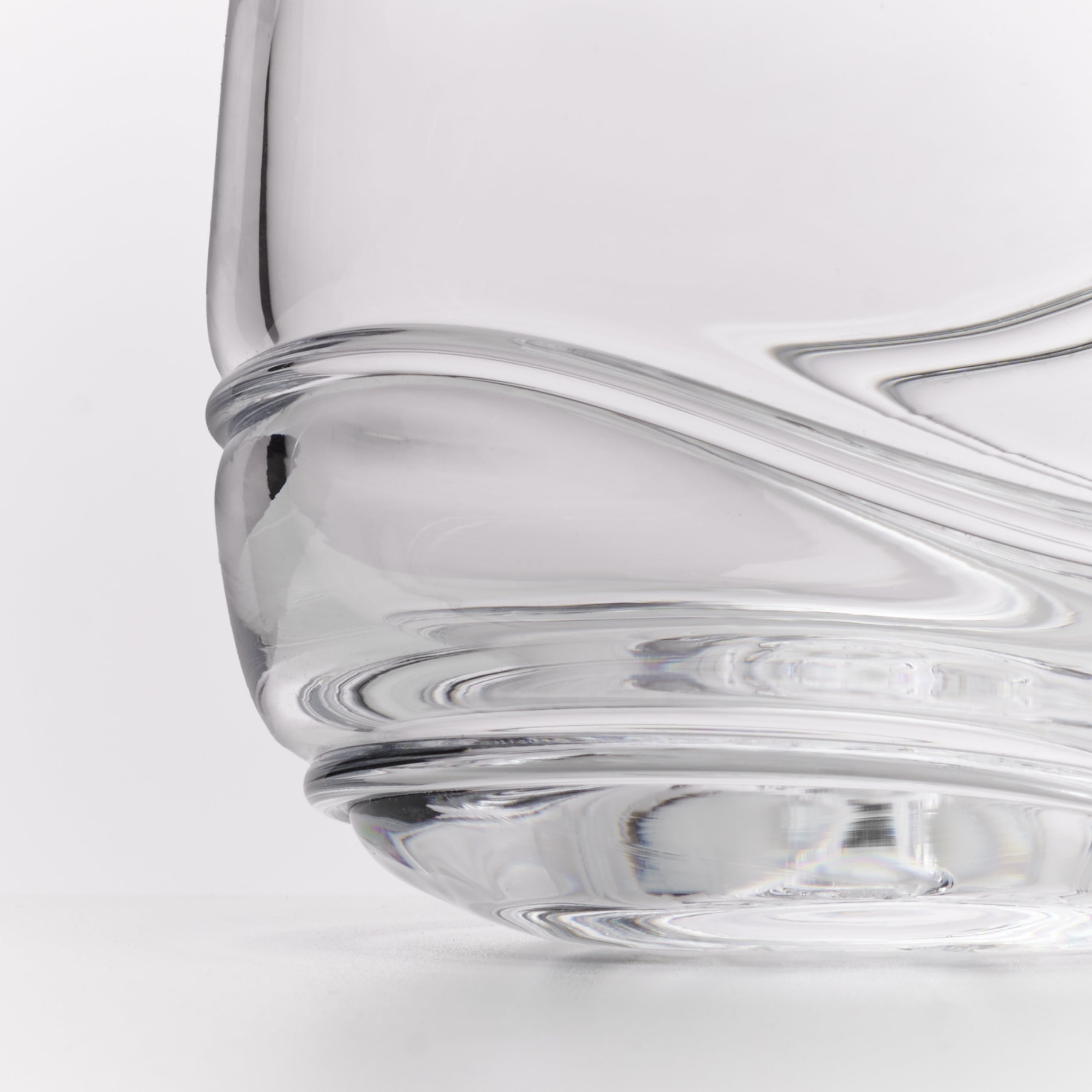Close-up of a clear glass with a sculptural, wavy ribbed base on a white background.