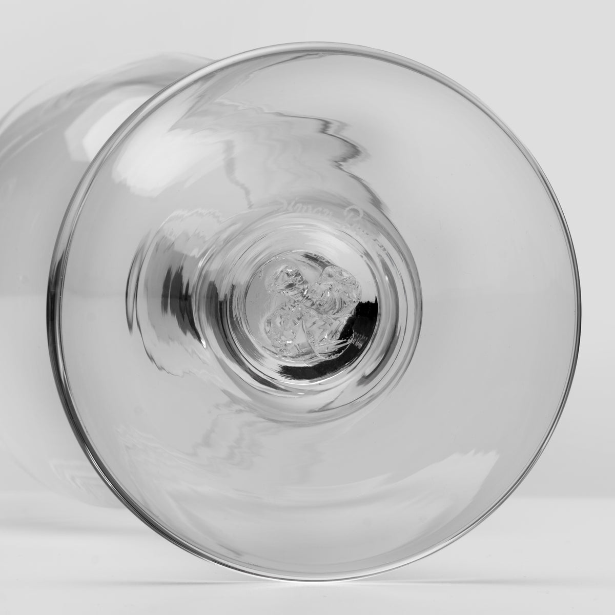 A close-up, bottom view of a clear glass drinking glass, on a light gray background.