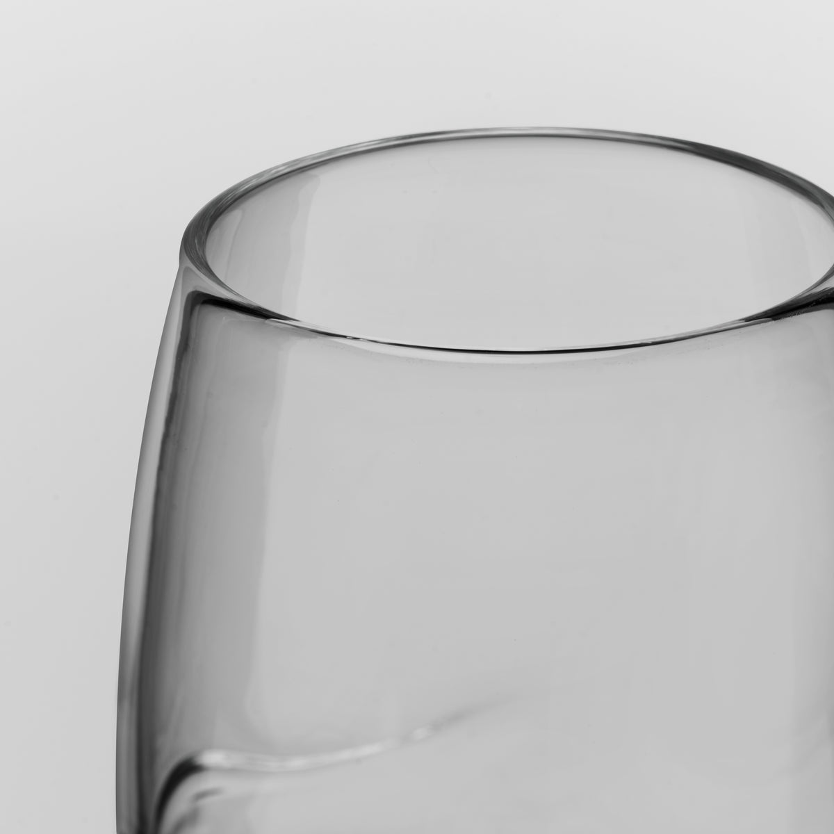 Close-up of a clear glass tumbler with a wide rim and smooth curved body, photographed against a light gray background.