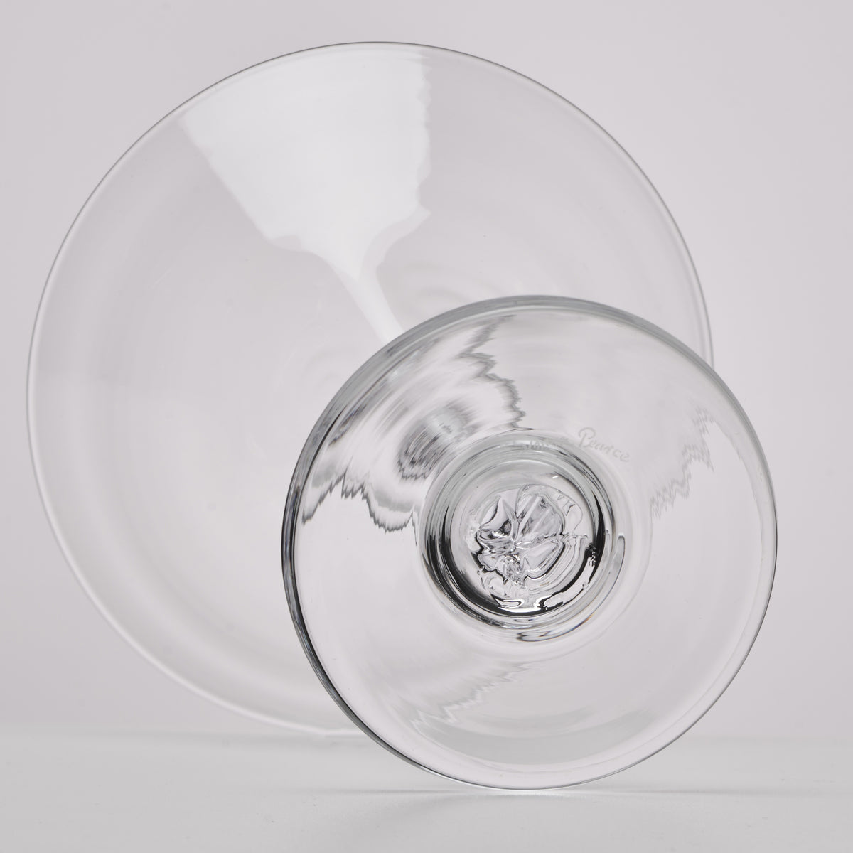 A clear glass bowl with a wide rim and a small pedestal base, photographed on a light gray background.