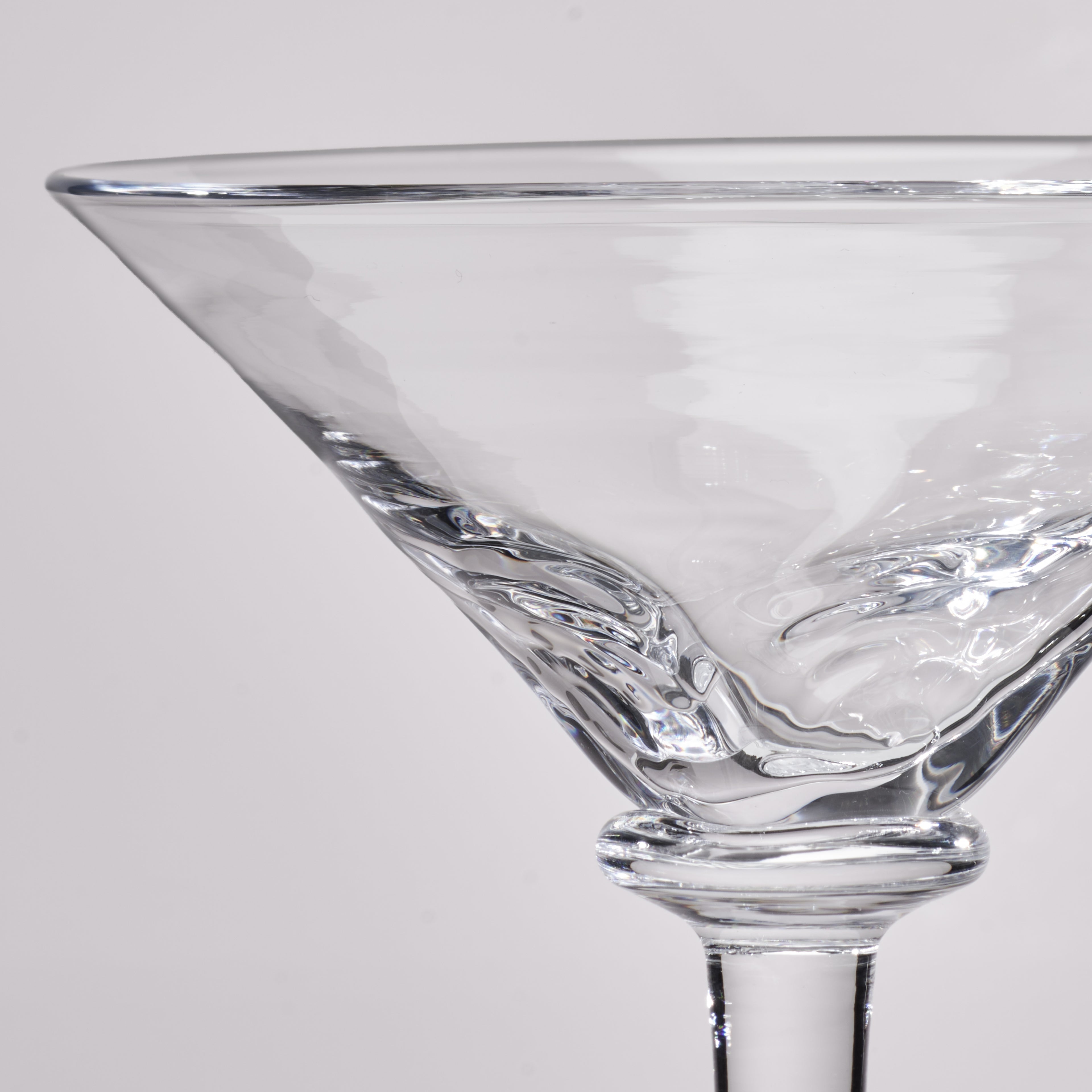 Close-up of a clear glass martini glass with a textured, wavy pattern on the bowl and stem, set against a light gray background.