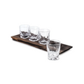 Four crystal rocks glasses with textured bases arranged on a dark wooden serving board.