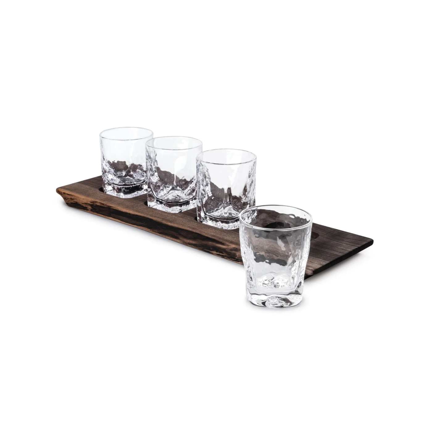 Four crystal rocks glasses with textured bases arranged on a dark wooden serving board.
