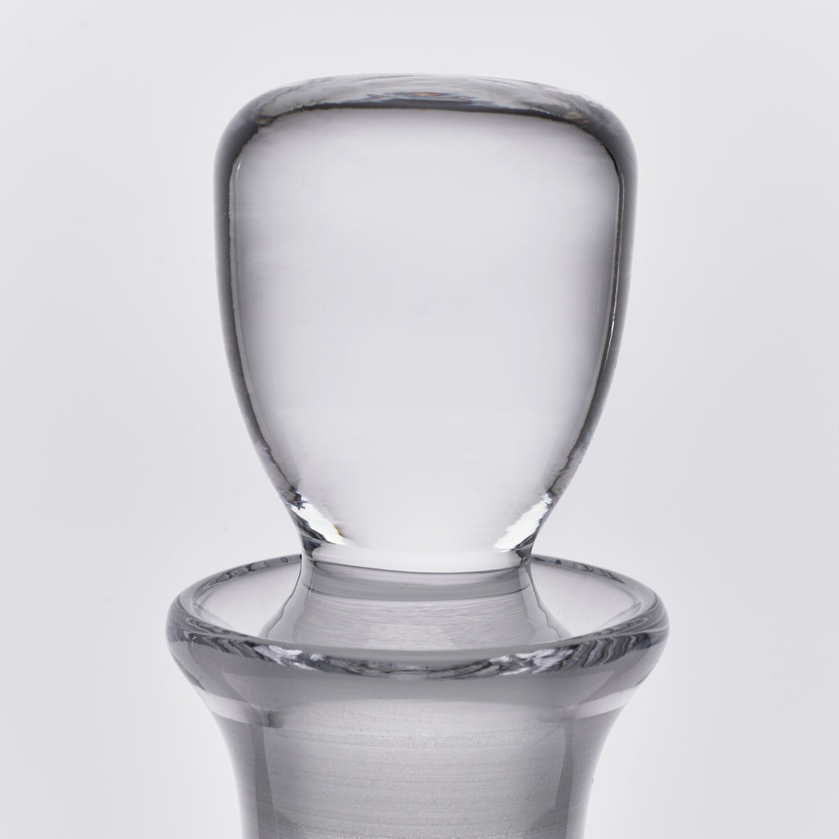 Clear glass decanter with rounded shoulder, tapered neck, and polished stopper featuring a wide base rim.
