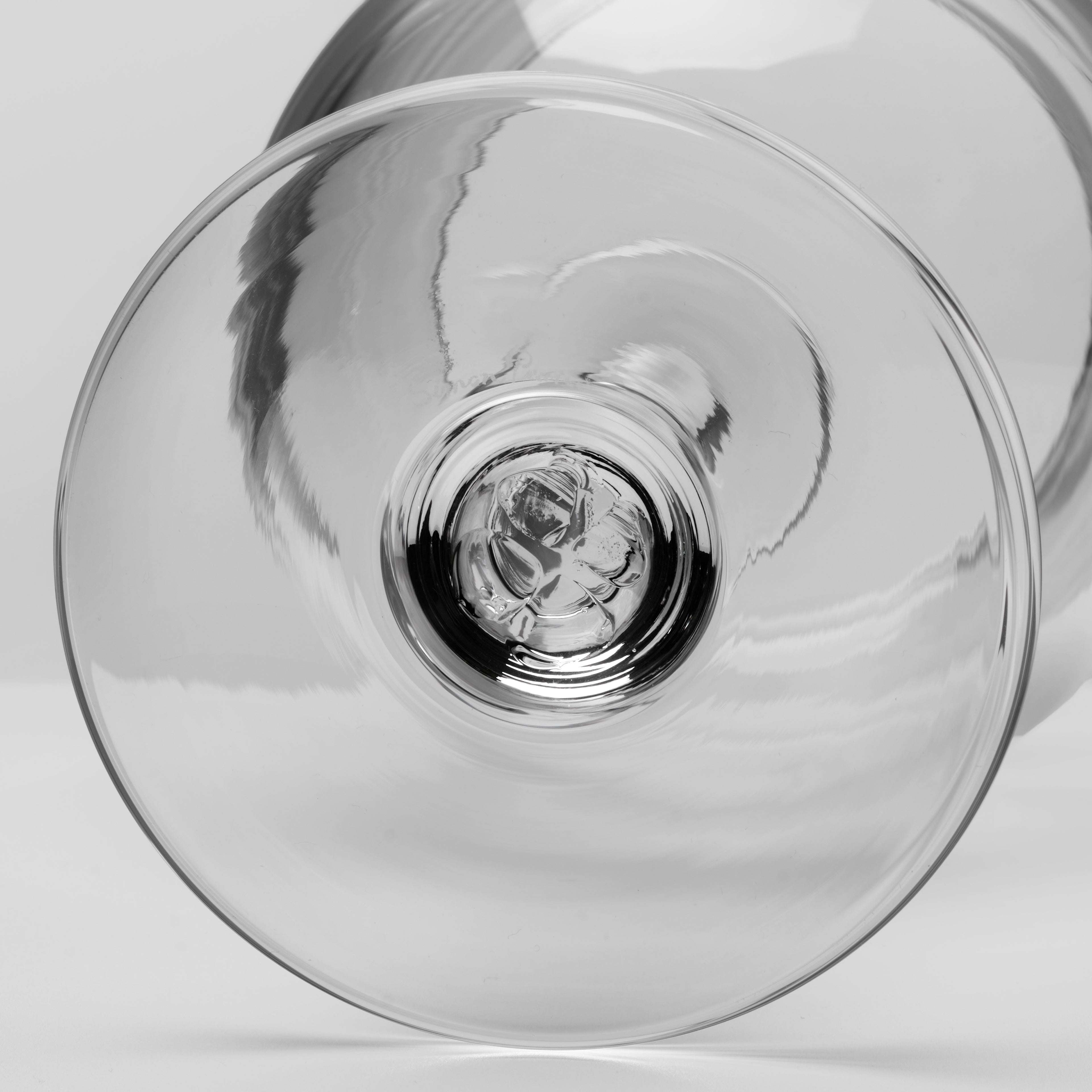 A close-up studio shot of a clear glass wine glass viewed from underneath, showing the circular bowl and stem base on a light gray background.