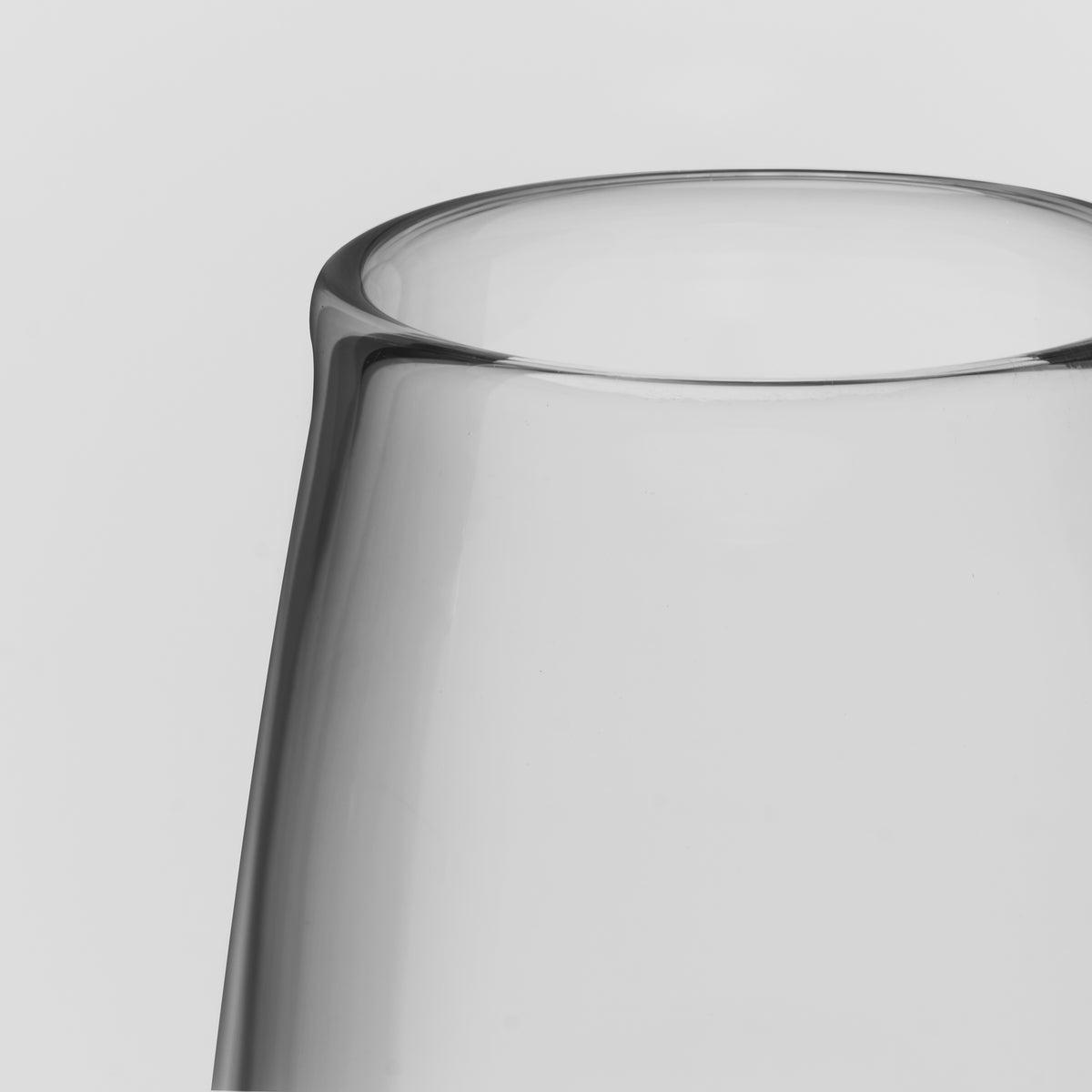 Close-up of a clear glass vessel, showing the smooth curved rim and transparent body against a light gray background.