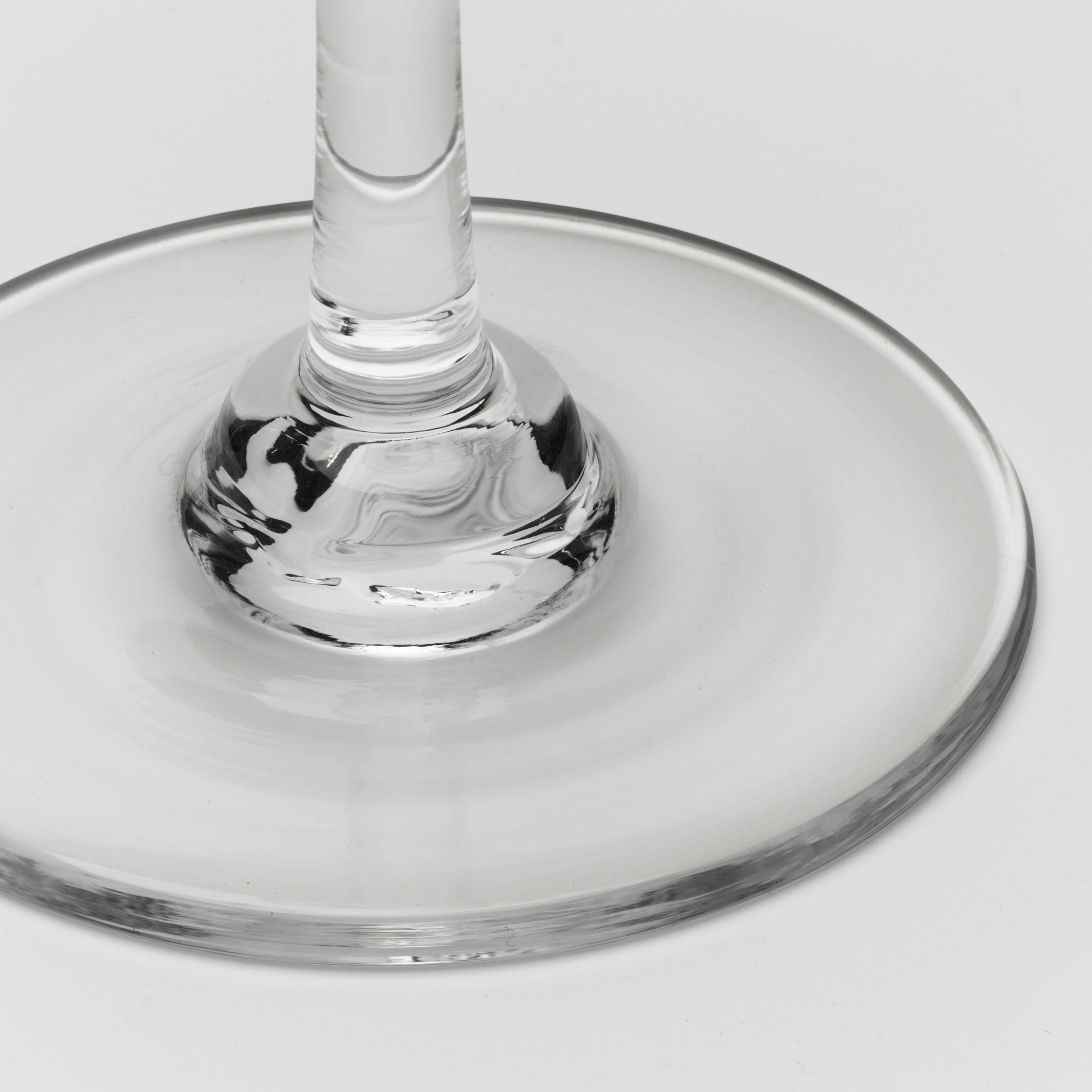 Close-up of a clear glass wine glass base and stem on a light gray background.