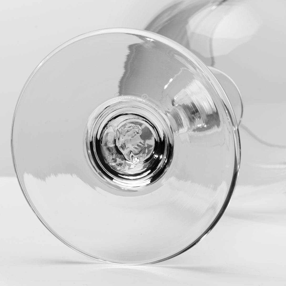 A close-up studio shot of a clear glass cocktail glass, showing the base and stem against a light gray background.