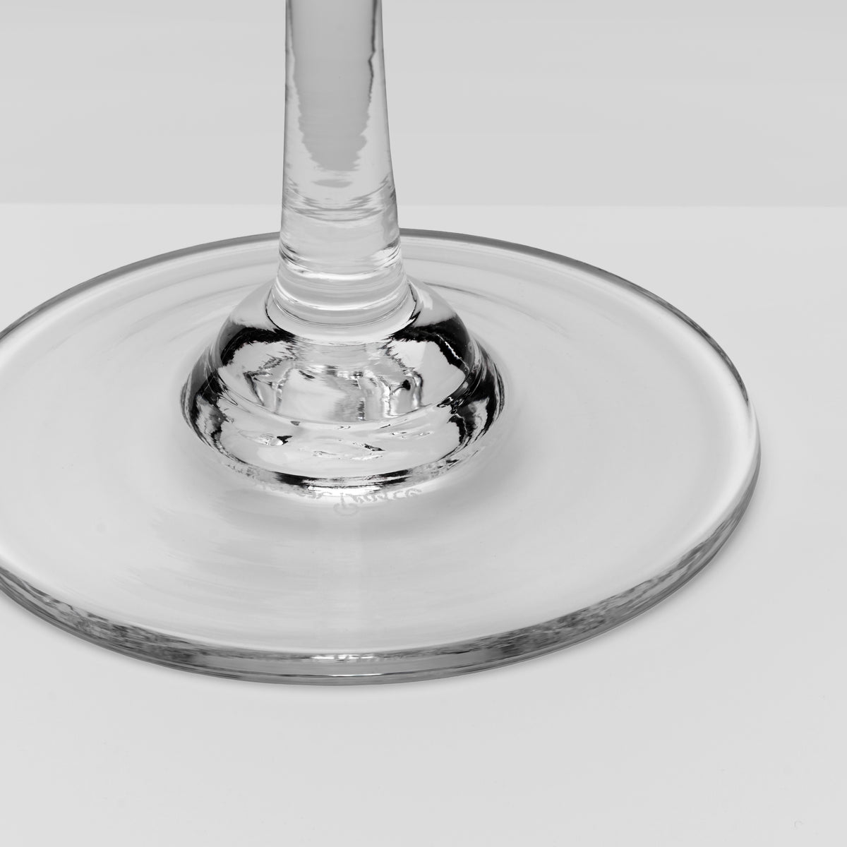A close-up of a clear glass wine glass base and stem on a light gray background.