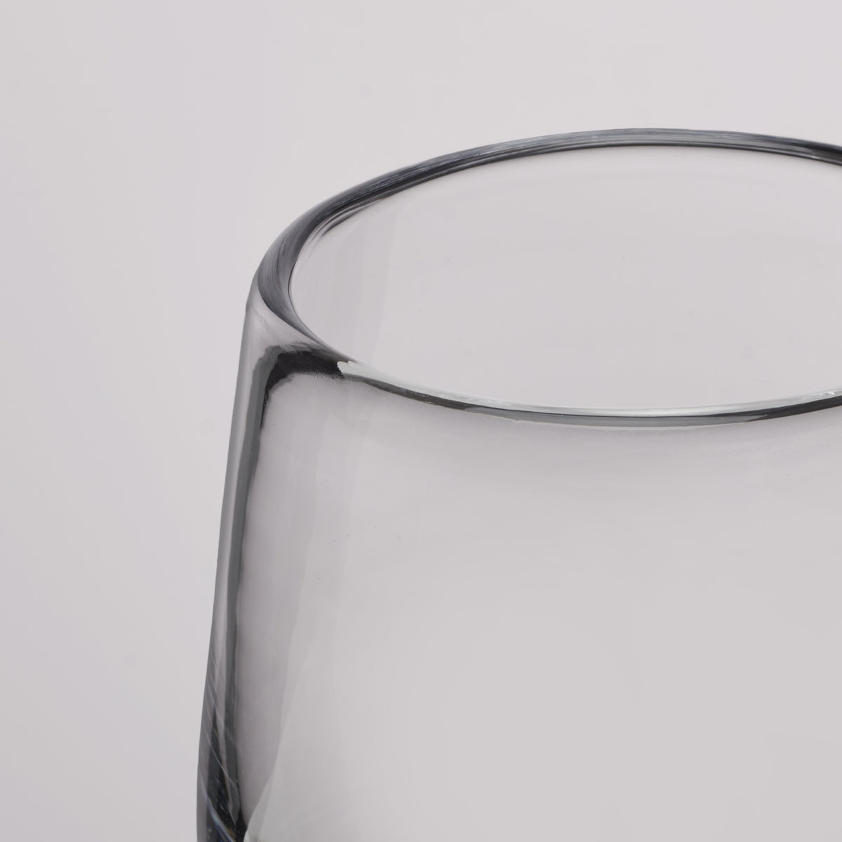 Close-up of a clear glass tumbler with a thick, rounded rim on a light gray background.