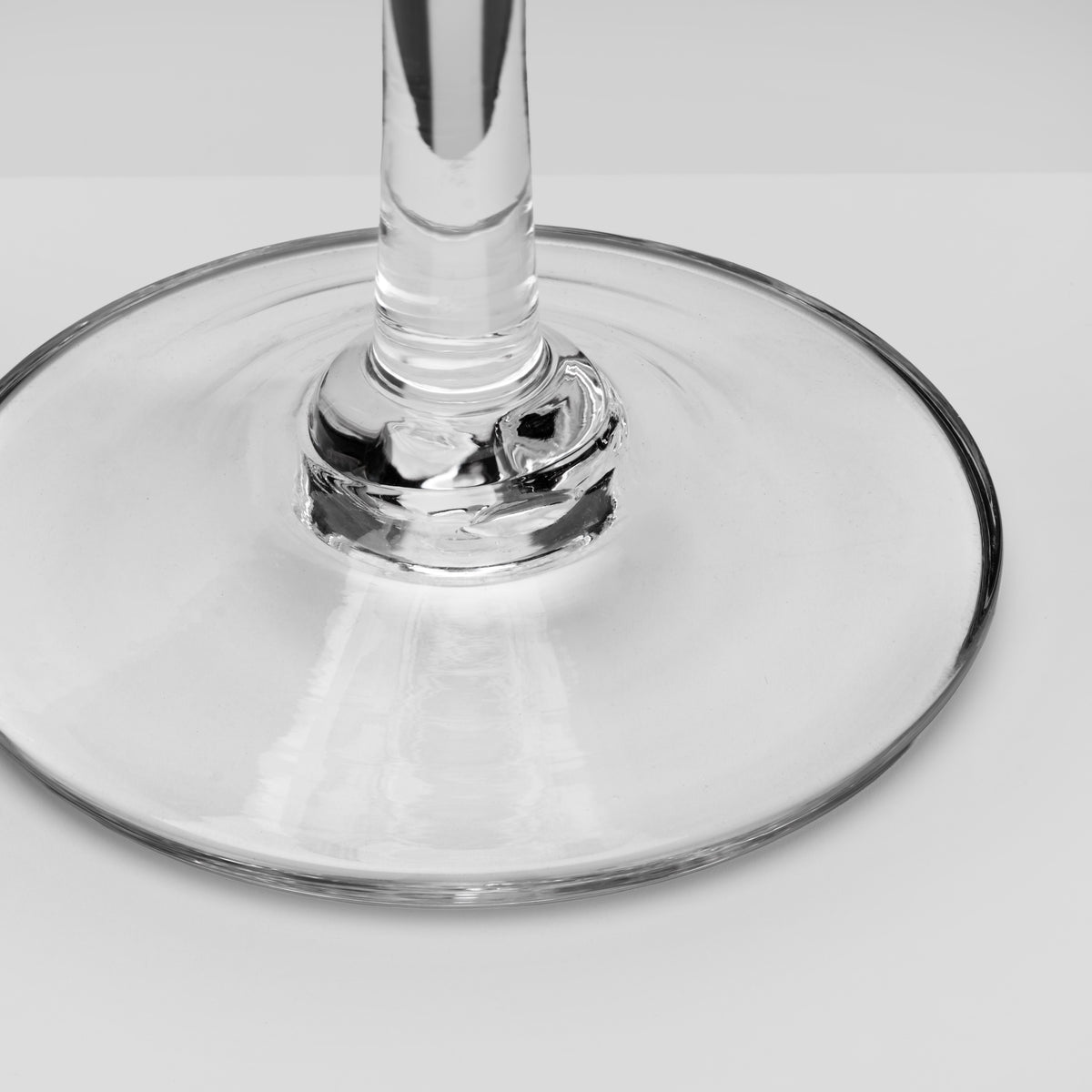 Close-up of a clear glass wine glass base and stem on a light gray background.