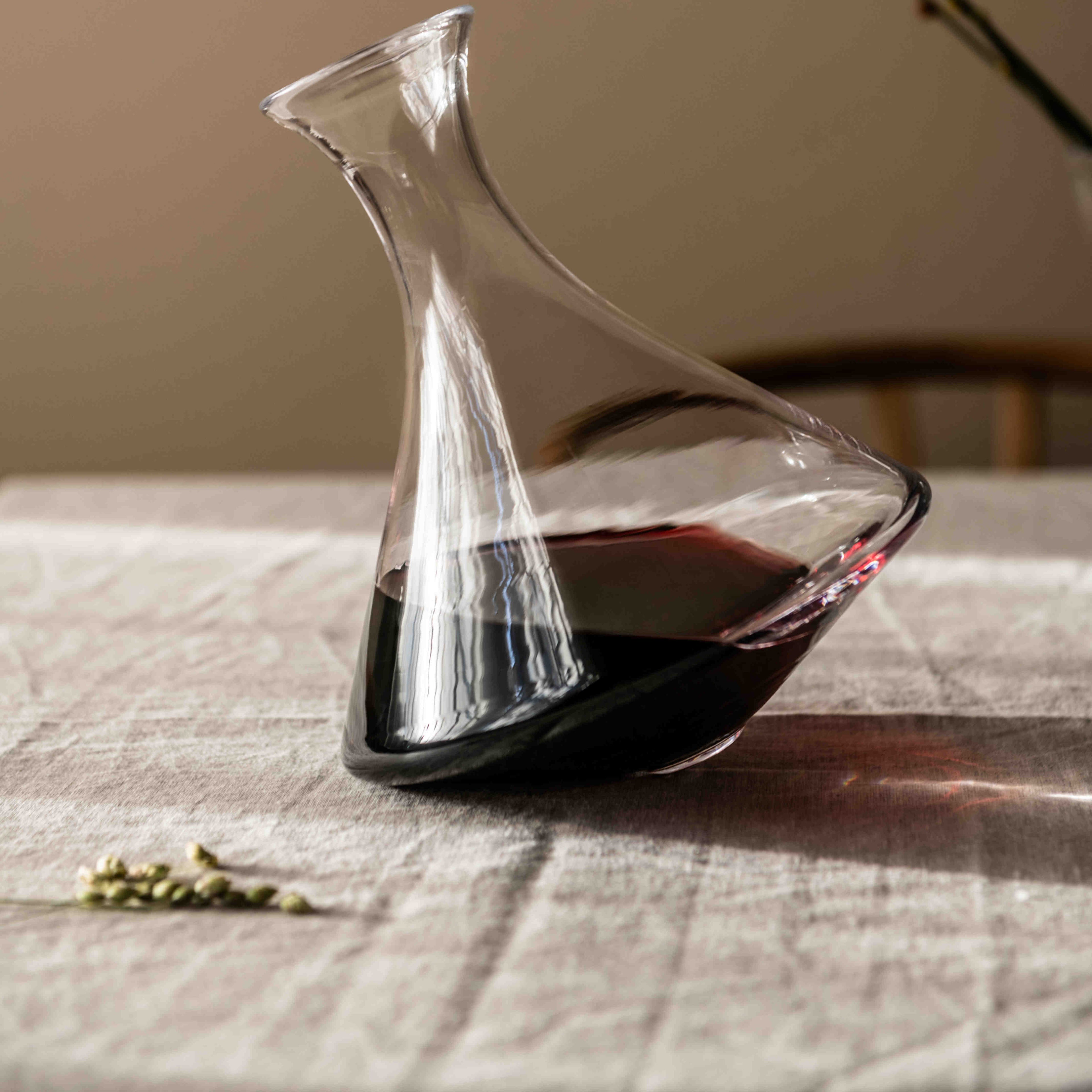 Clear glass wine decanter with curved spout and tilted base containing red wine.