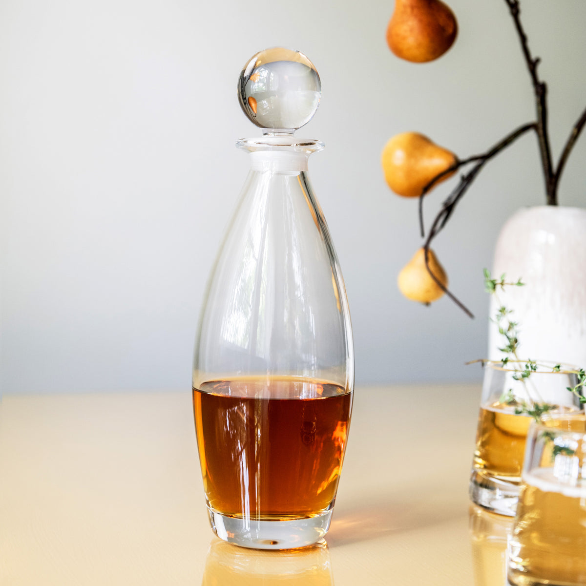 Clear glass decanter with spherical stopper, filled with amber liquid.