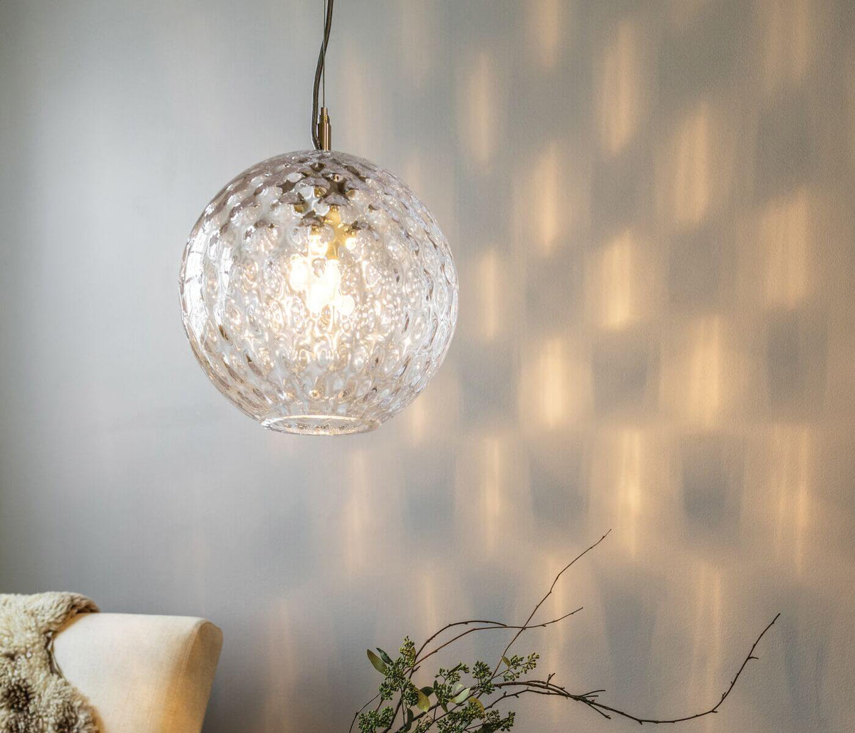 Clear textured glass globe pendant with metal chain casting light patterns on wall.