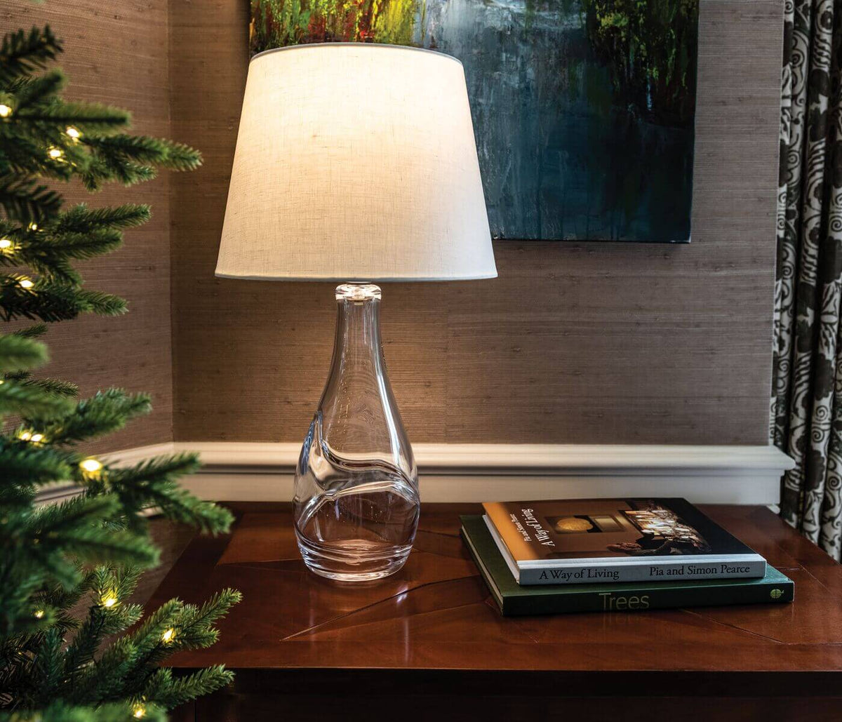 Clear glass bottle-shaped base with cream linen tapered shade on wooden side table.