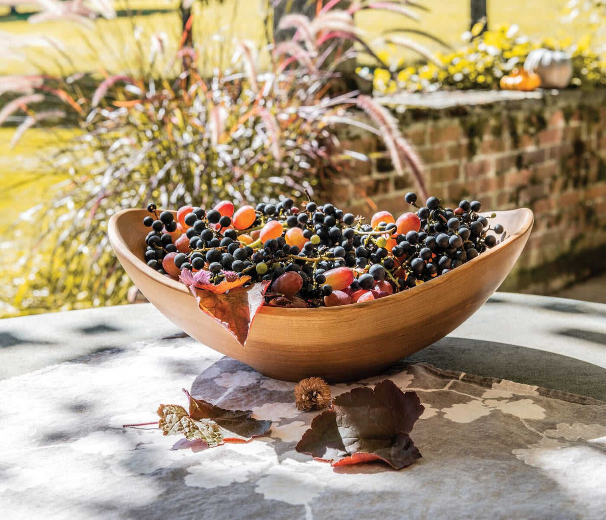 Wooden bowl with live edge containing mixed berries, displayed outdoors on stone surface.