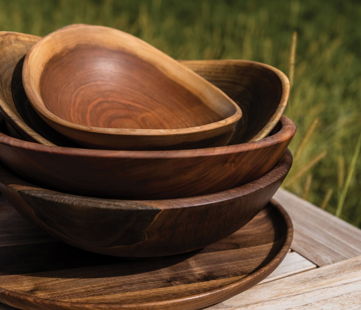 Stacked wooden bowls with natural live edges in varying shades of brown, displayed outdoors on a wooden surface.