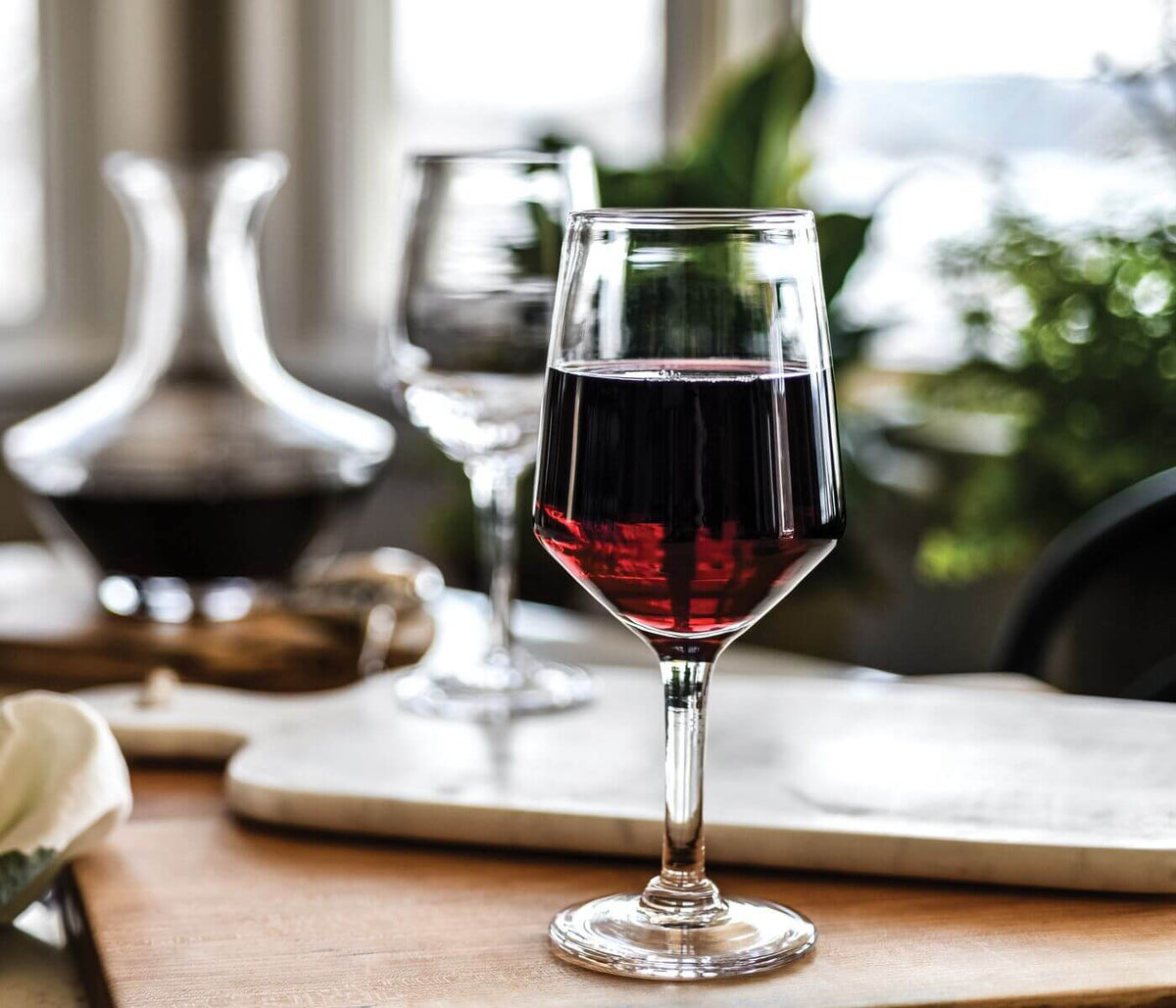 Red wine poured into glass with decanter and second glass in background on table setting.