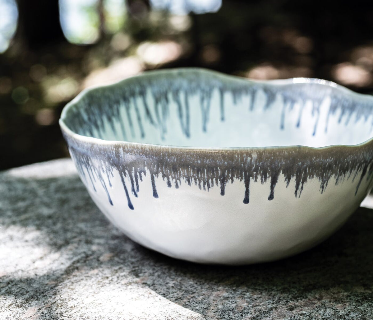 White ceramic bowl with blue drip pattern and wavy rim, shown from above on stone surface.