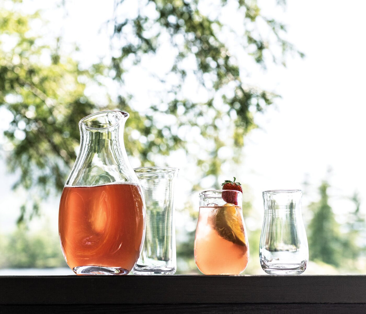 Glass carafe filled with amber liquid alongside empty drinking glasses on a black surface.