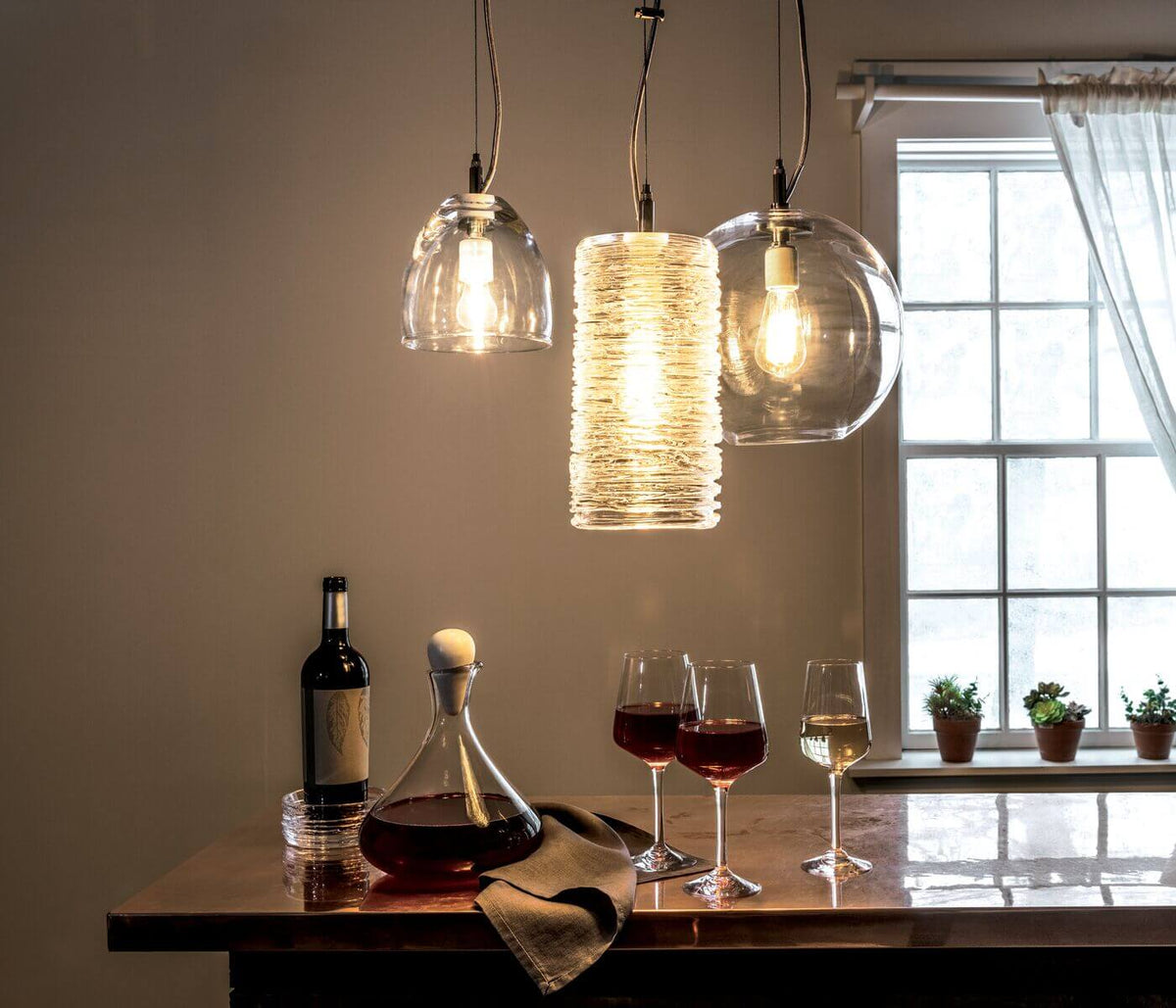 Three hanging glass pendant lights with brass fittings suspended above a dining table.