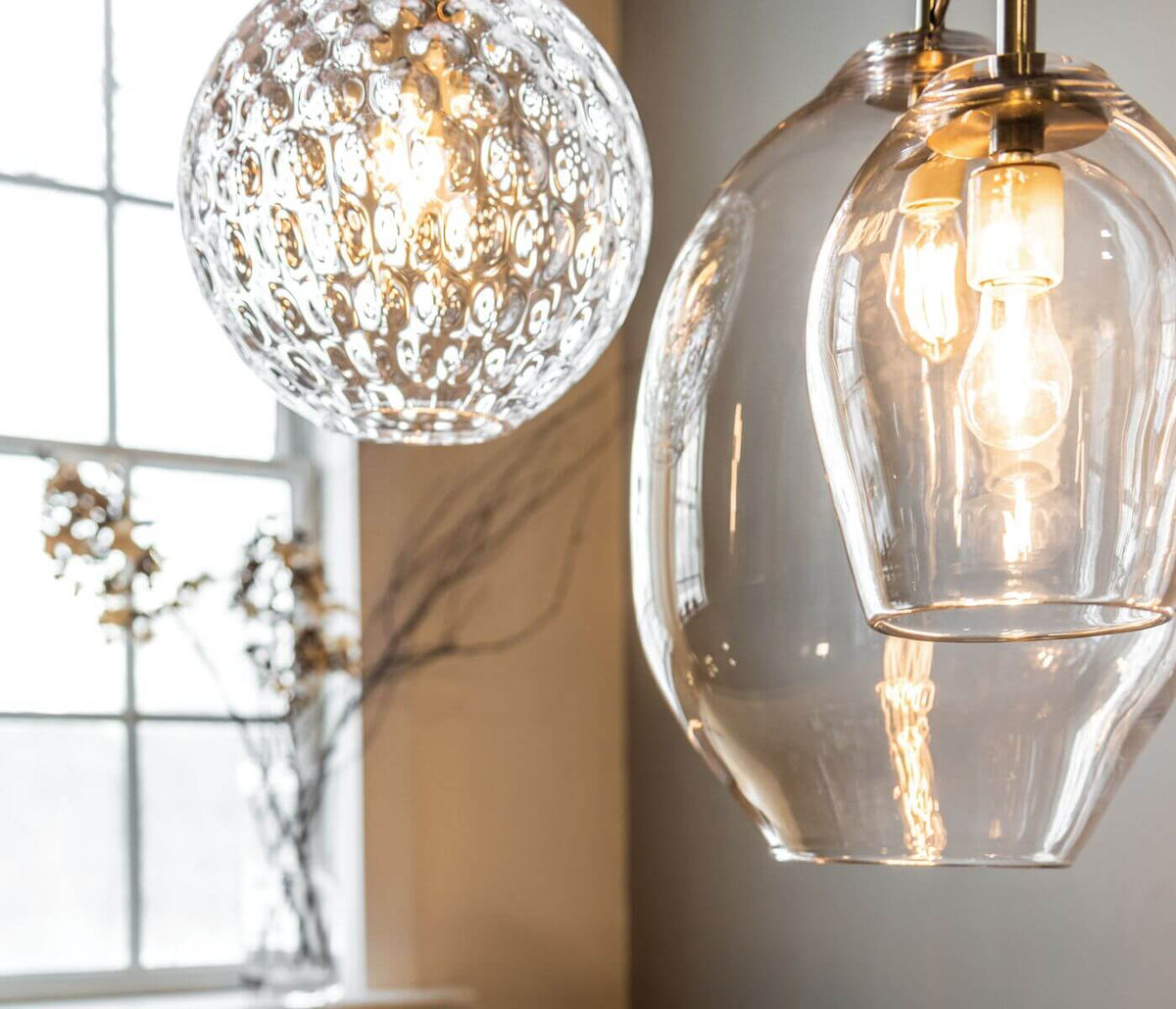 Two hanging pendant lights with clear glass shades and brass hardware, one with textured pattern and one smooth, illuminated 