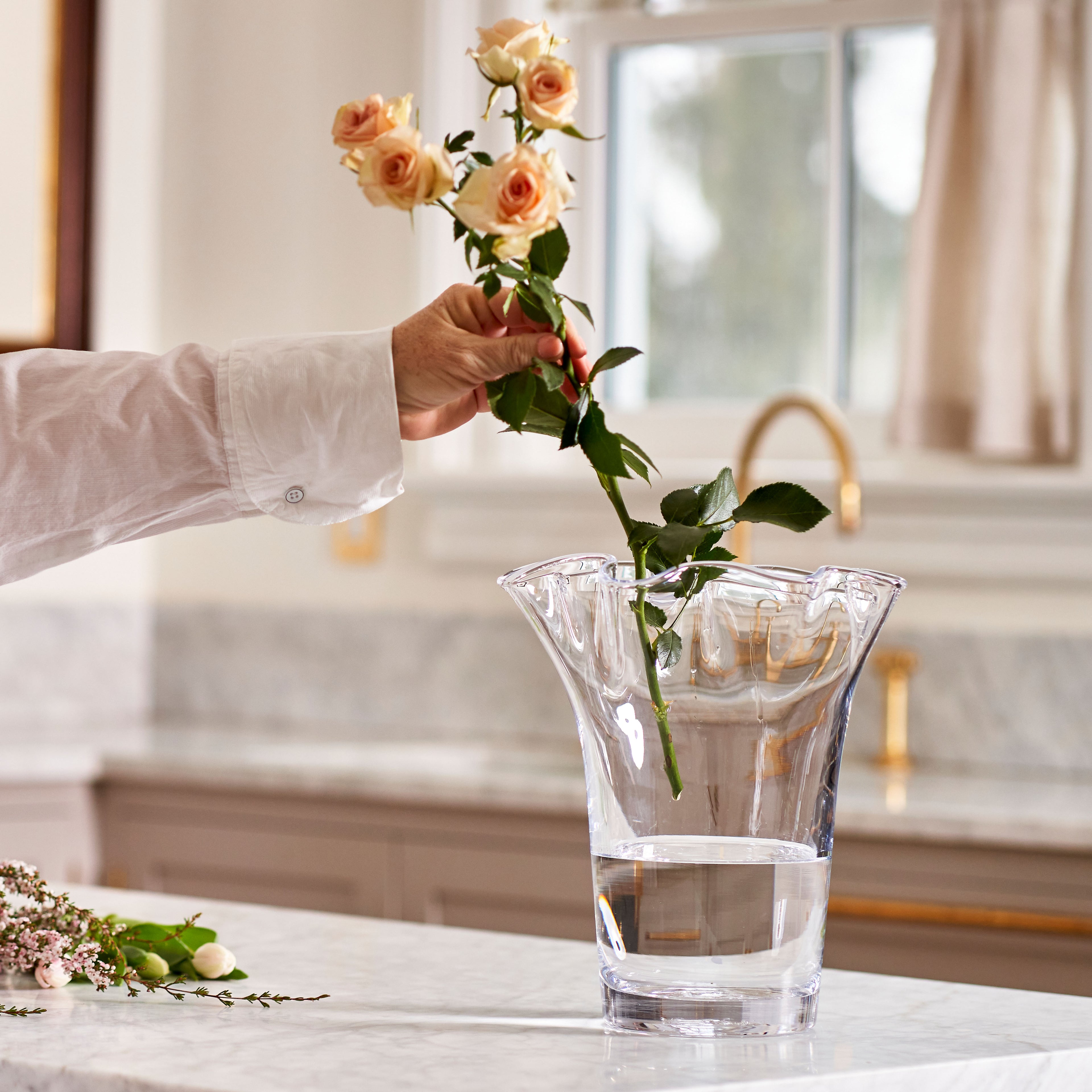Clear glass vase with wavy edges holding peach roses and green stems, displayed with water.