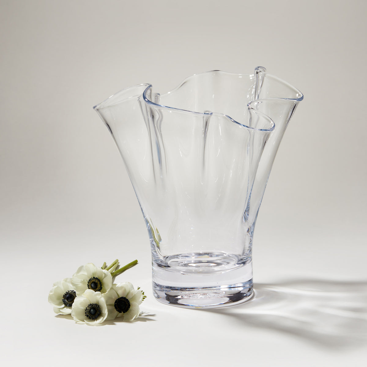Clear glass vase with wavy fluted edges and blue accent lines, shown with white anemone flowers.