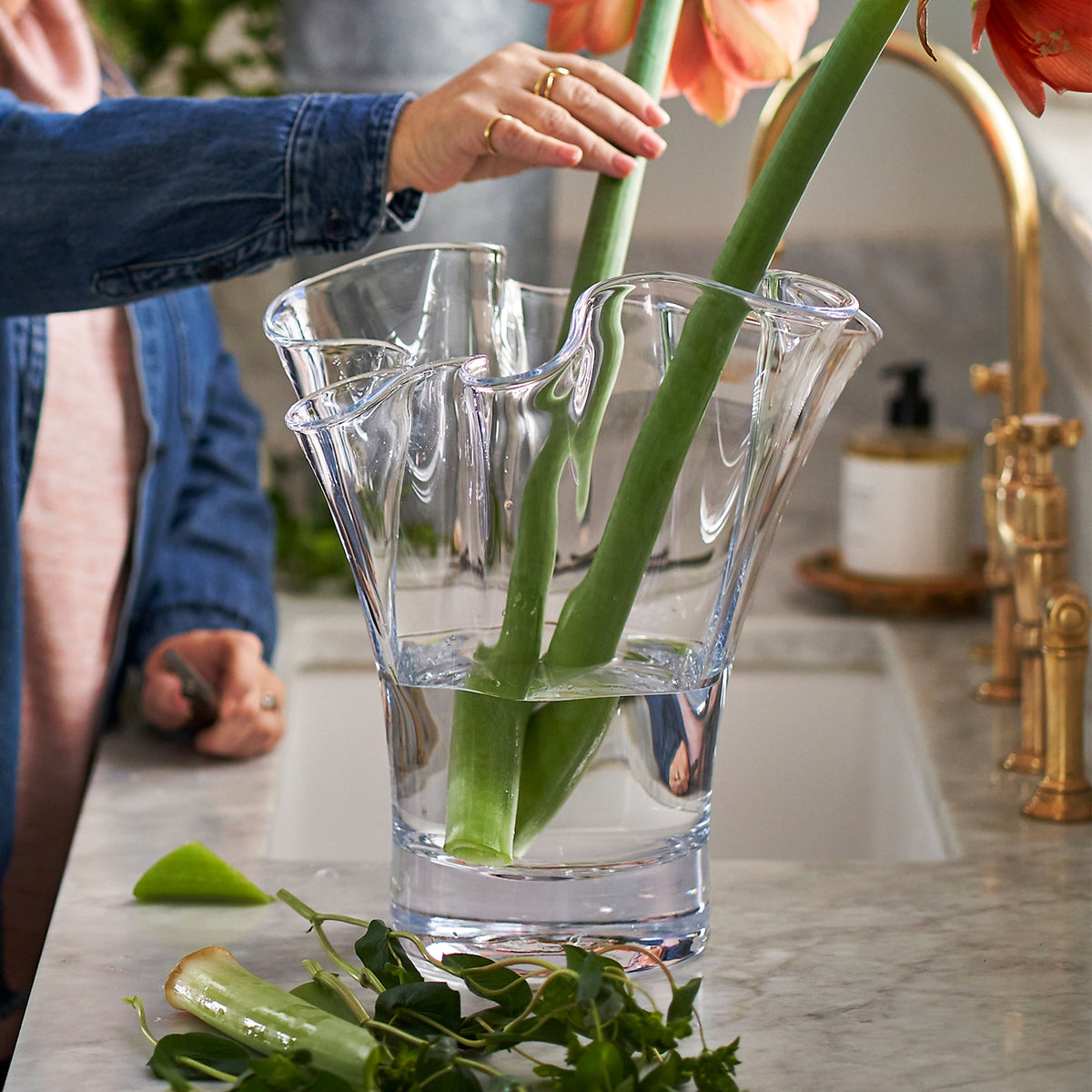 Clear glass vase with wavy ruffled edges holding green stems and red anemone flowers.