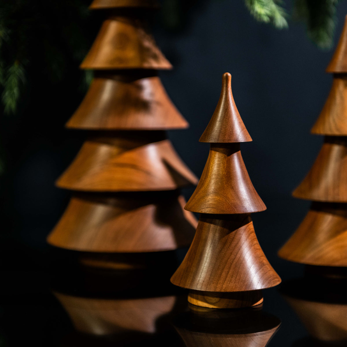Stacked wooden cone-shaped trees in cherry wood with dark finish against navy background.